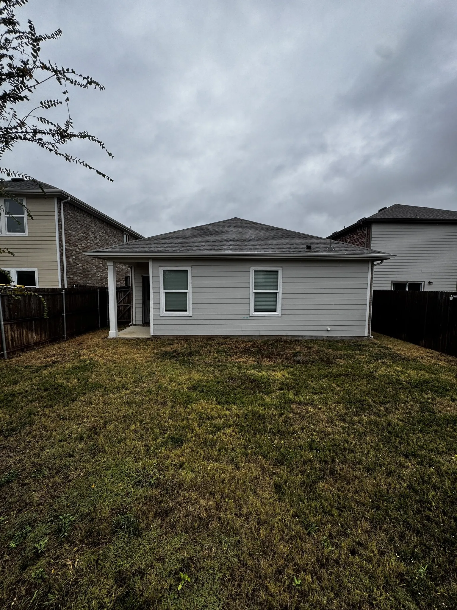 Rear elevation featuring light gray siding, a covered patio, and a shingle roof