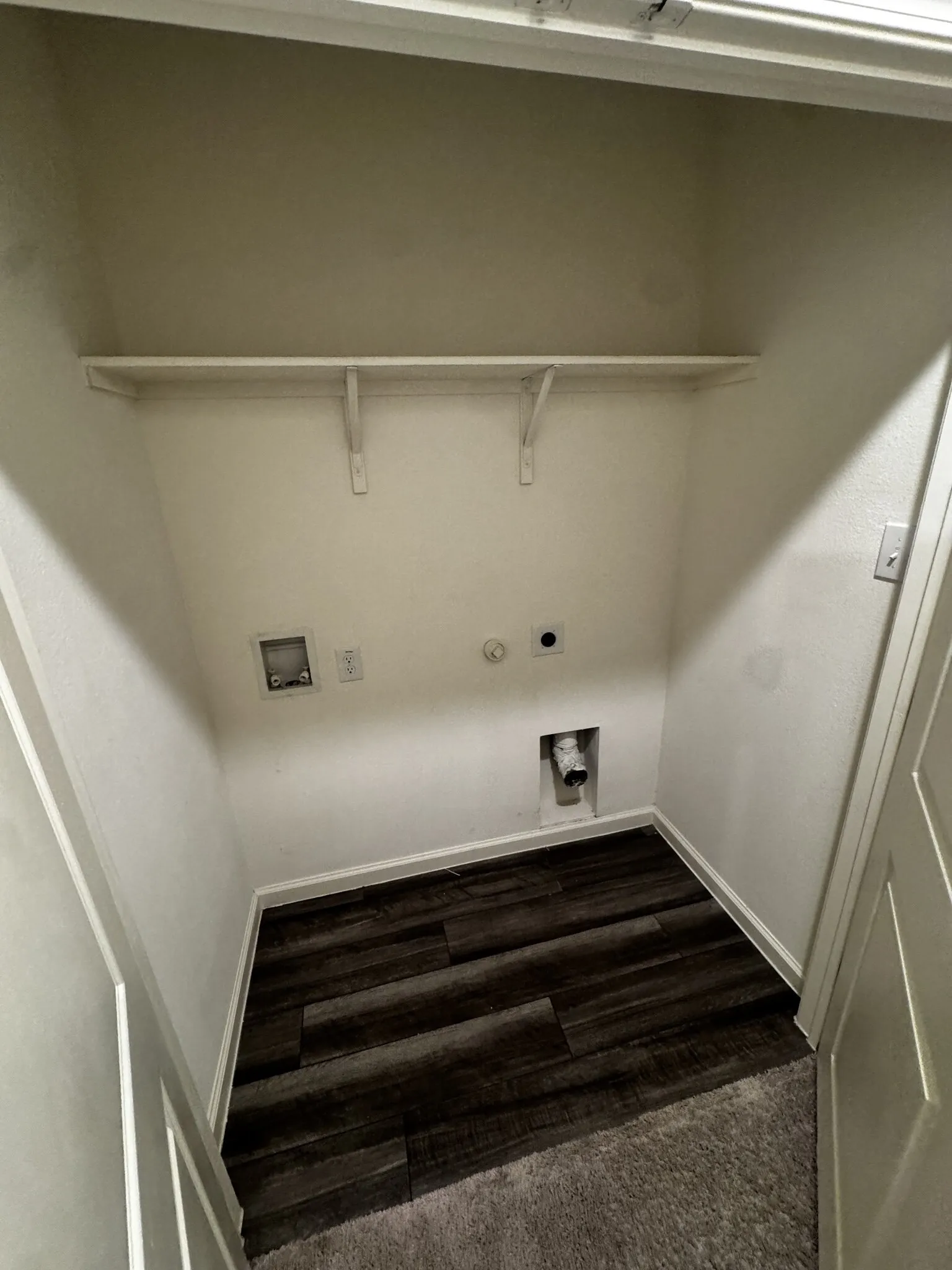 Utility alcove featuring a built-in shelf, dark wood-finish flooring, and white walls