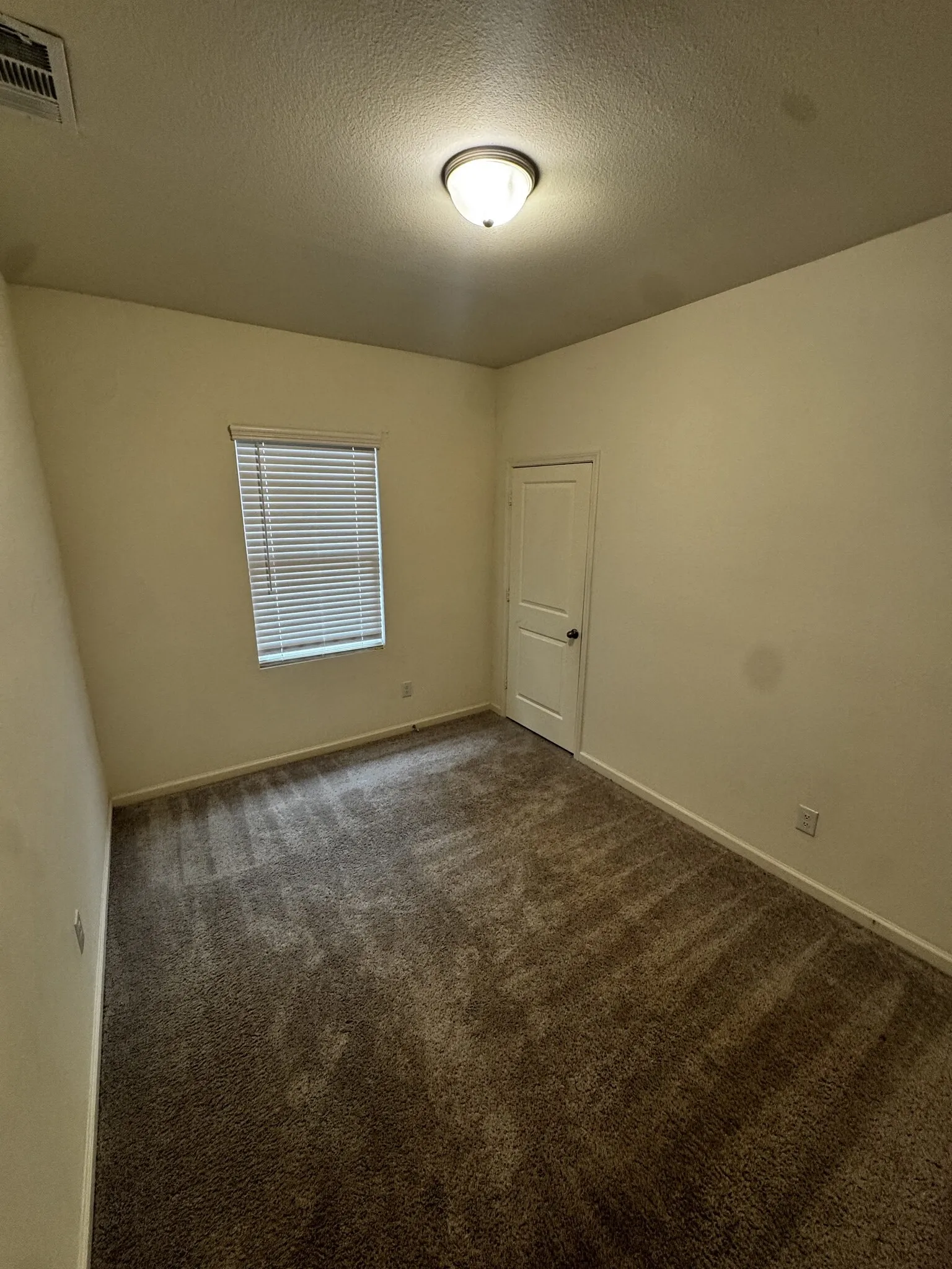 Neutral tone wall paint with a textured ceiling finish, recessed window with blinds, and flush-mount ceiling light