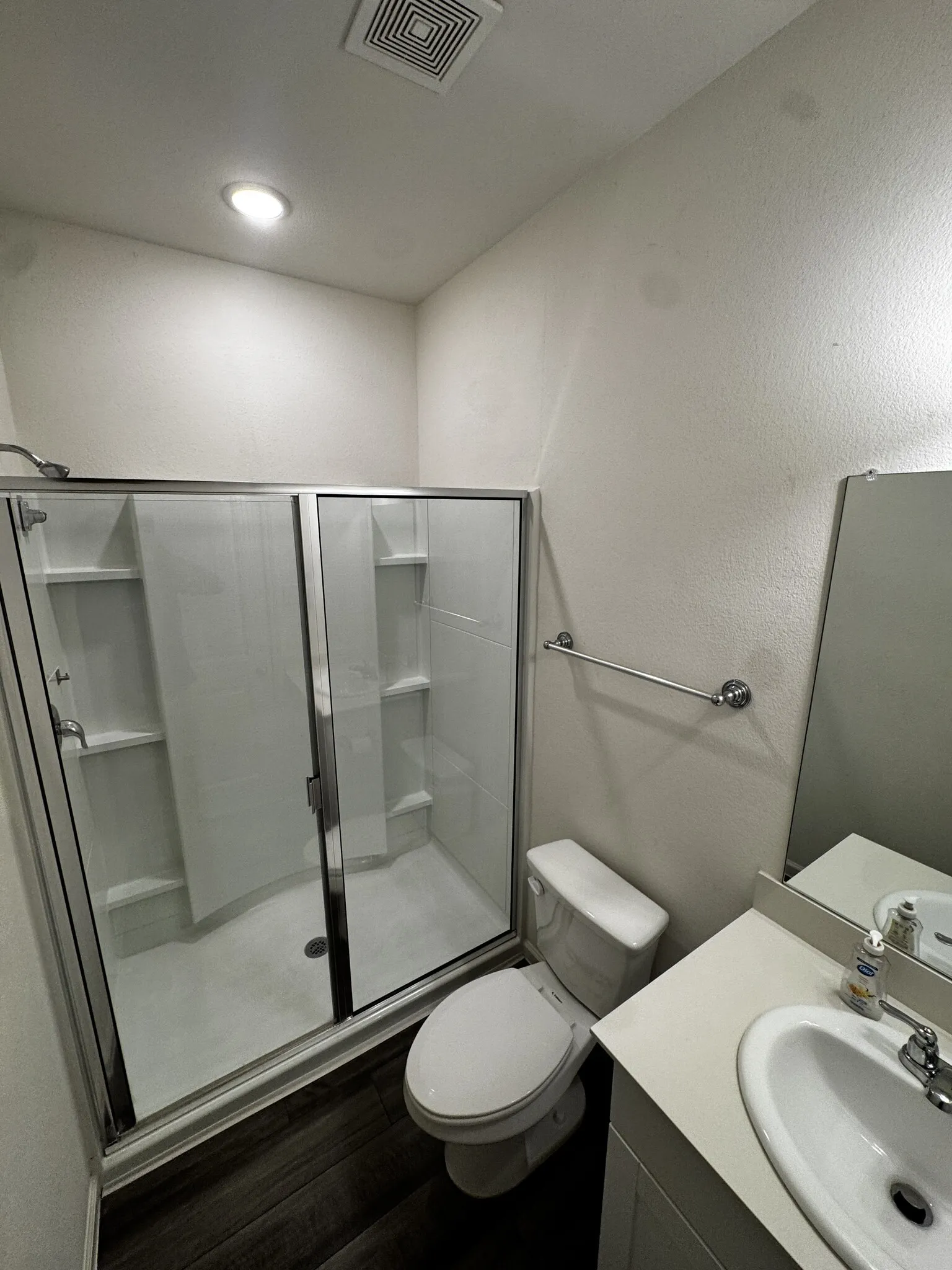 Shower with clear glass enclosure, white vanity with integrated sink, and dark wood-finish flooring