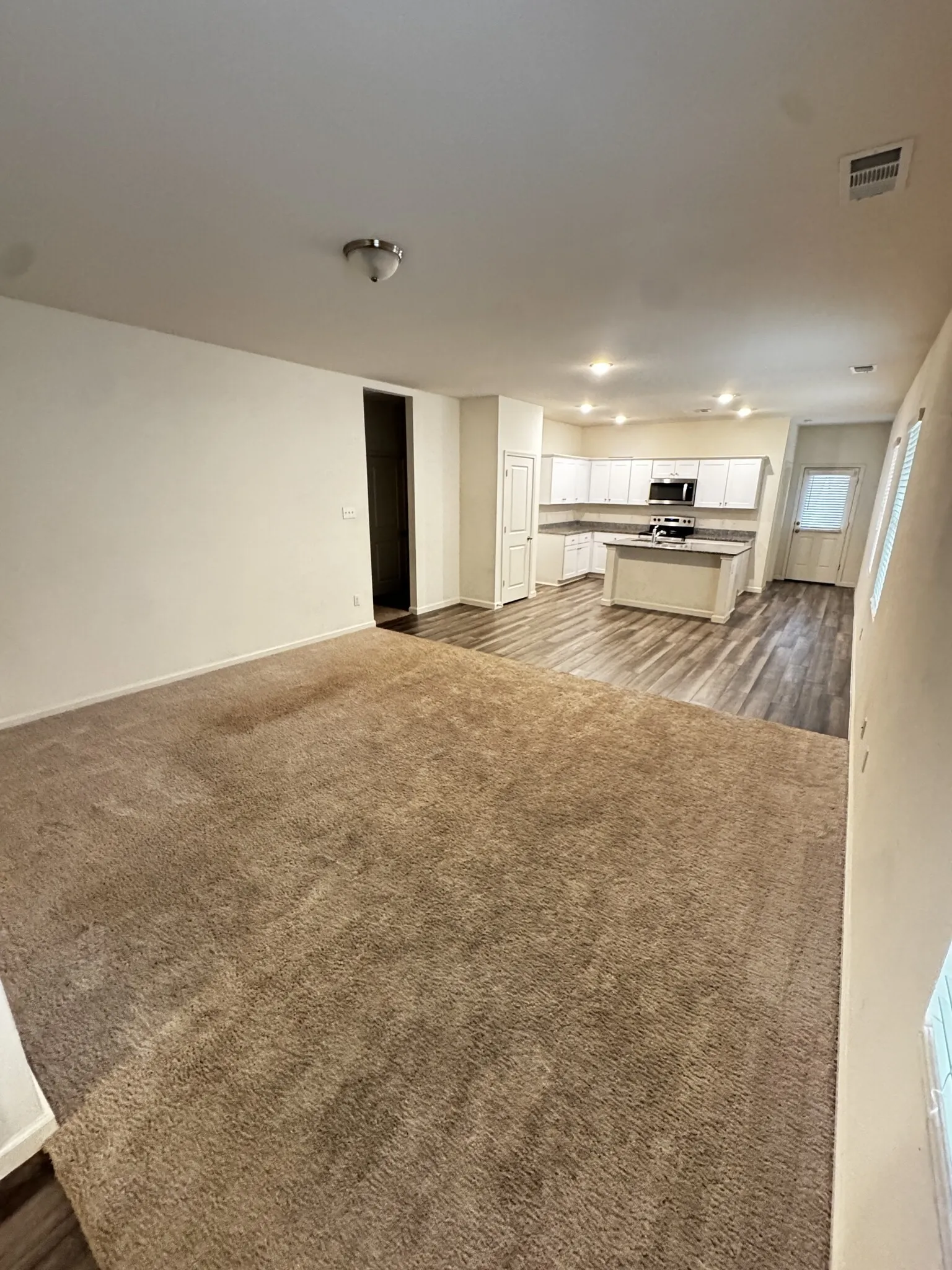 Open-concept living space featuring wood-finish flooring, recessed lighting, and a kitchen with white cabinetry and a central island