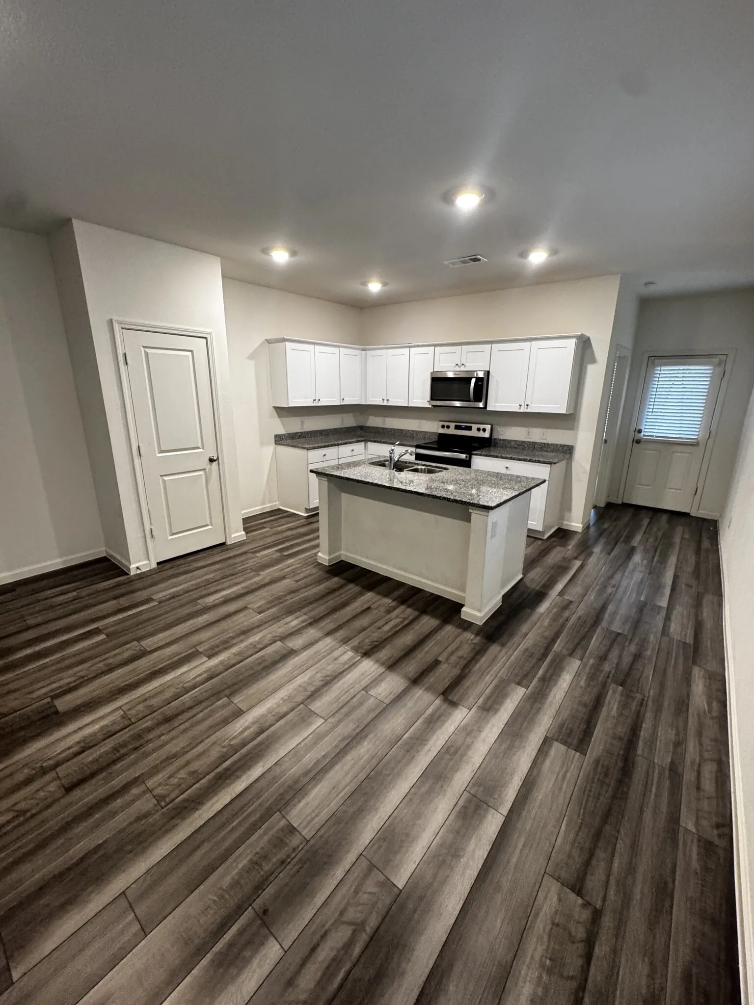 Open-concept kitchen with wood-finish flooring, white cabinetry, a central island, stainless steel appliances, and recessed lighting