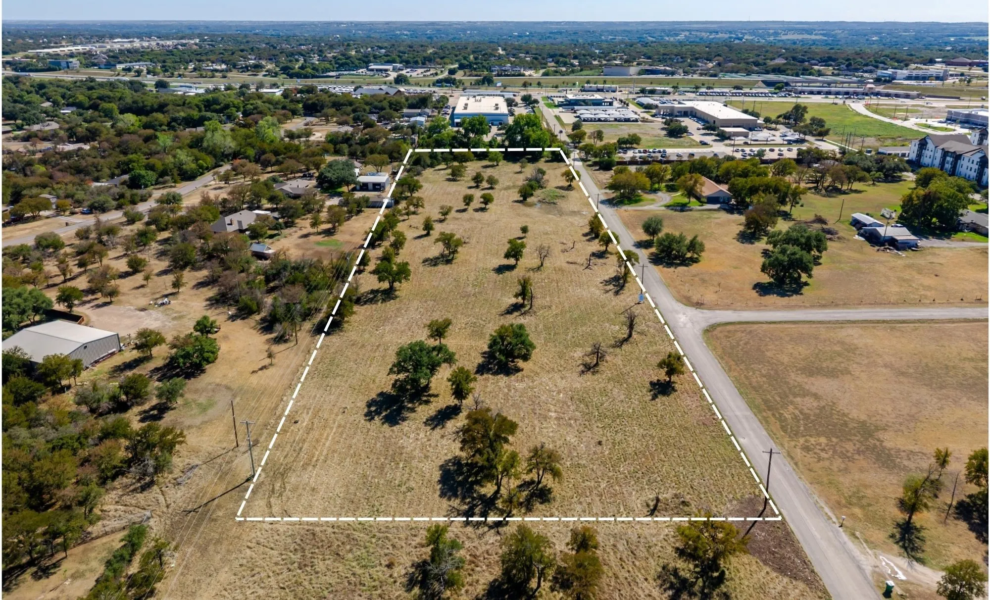 Expansive land parcel with mature trees and a paved road frontage