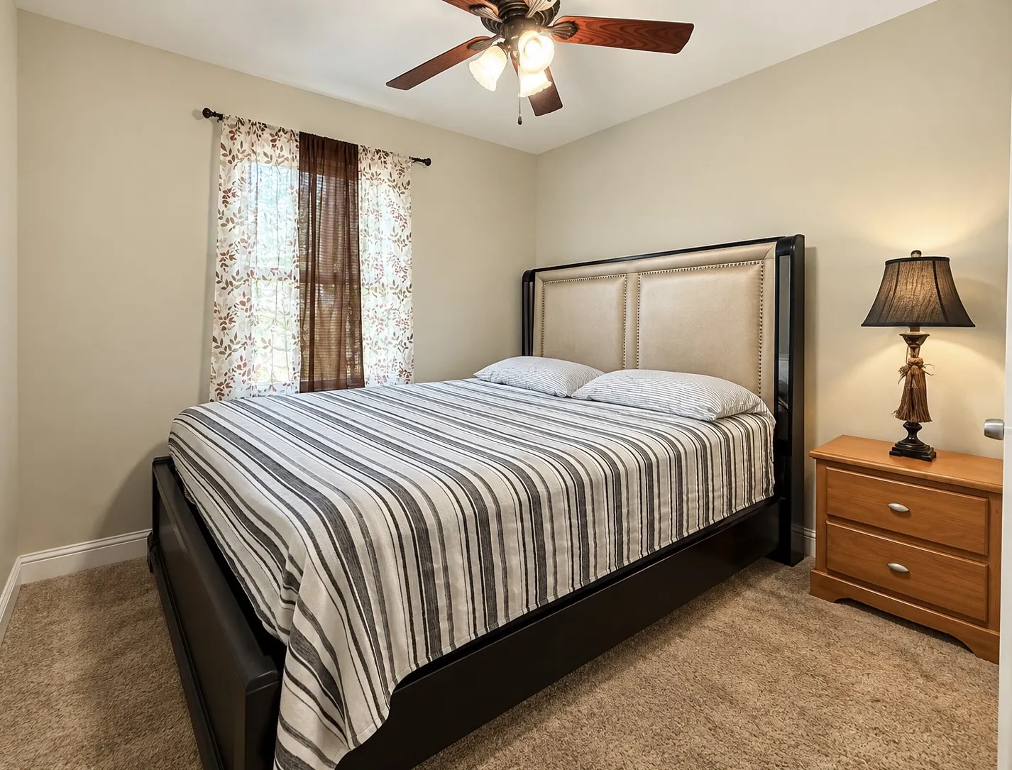Neutral wall color, ceiling fan with integrated lighting, window with curtain rod, and carpeted flooring