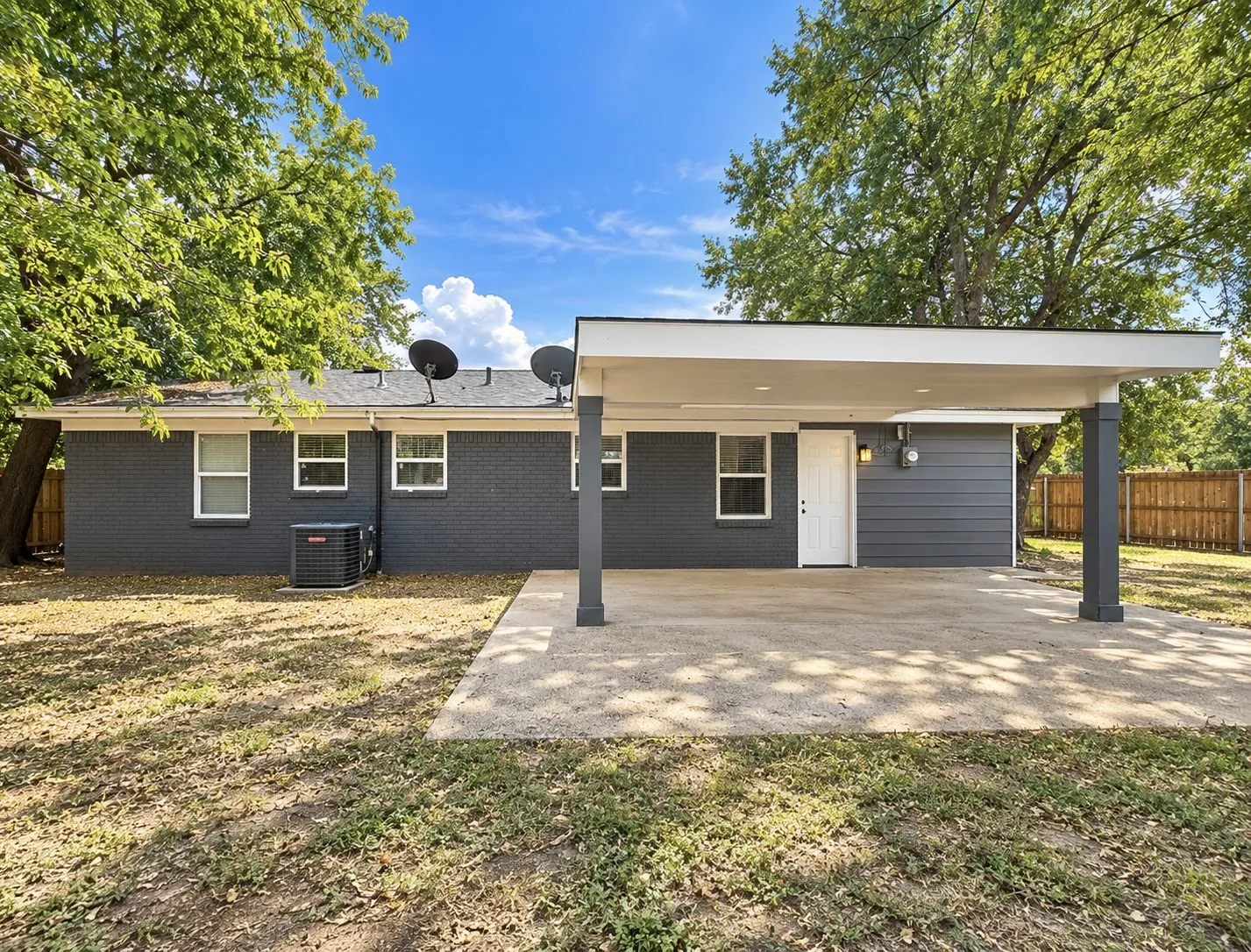 Expansive concrete patio with a covered outdoor area, dark gray exterior siding, and white trim windows