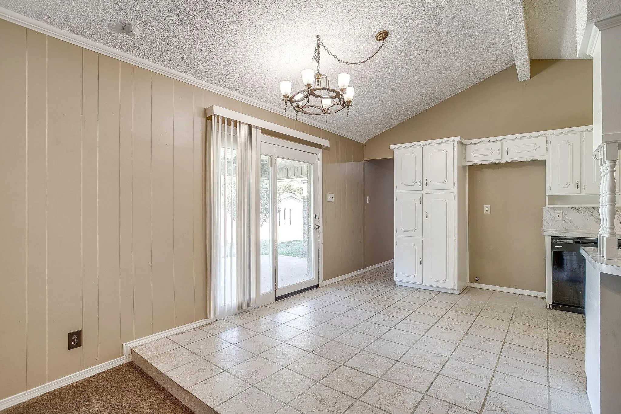 Vaulted ceiling with exposed beams, white paneled cabinetry, tile flooring, glass sliding door, and a chandelier lighting fixture
