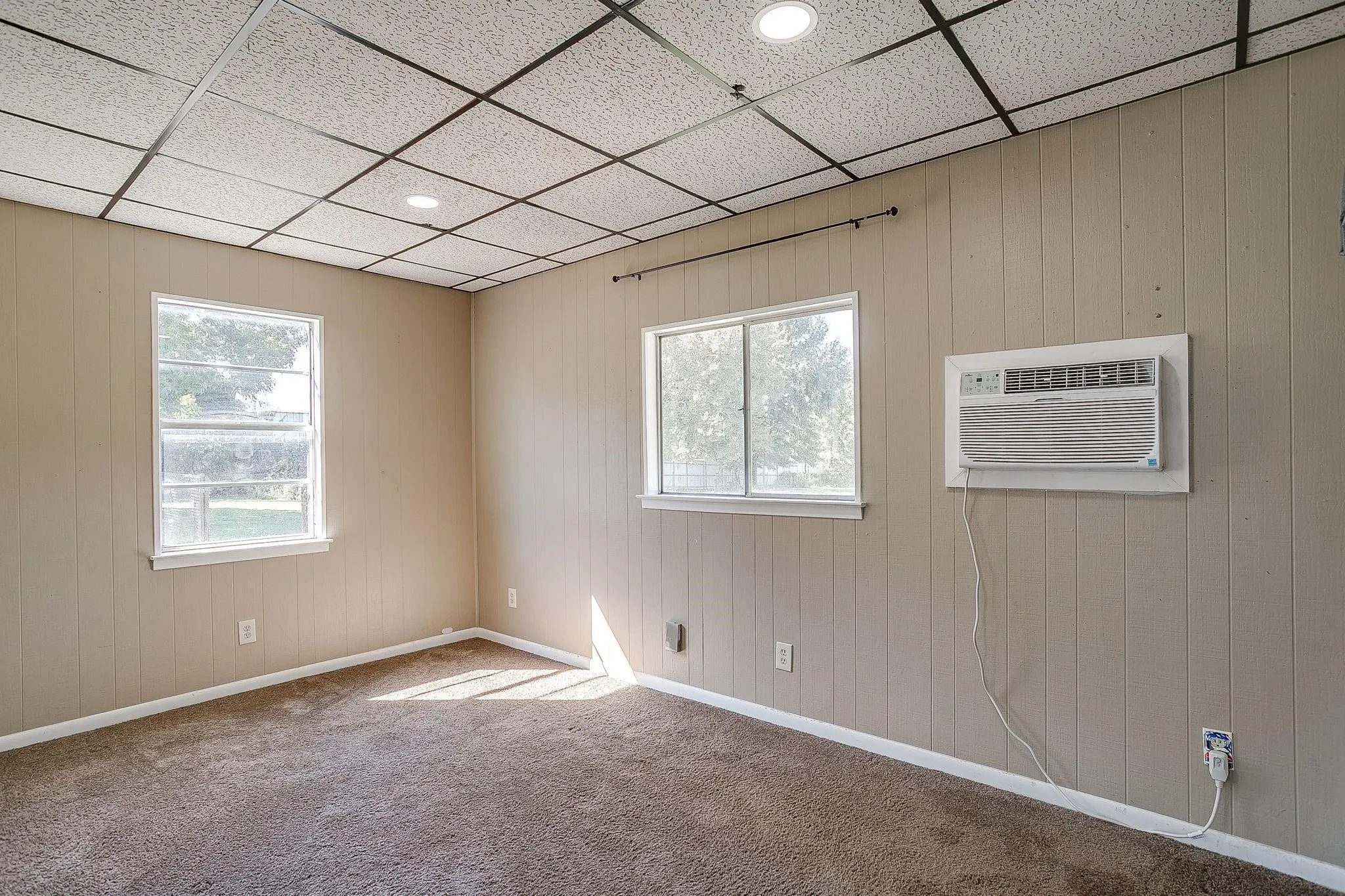 Carpeted flooring, two windows with white trim, recessed ceiling lighting, and a wall-mounted air conditioning unit