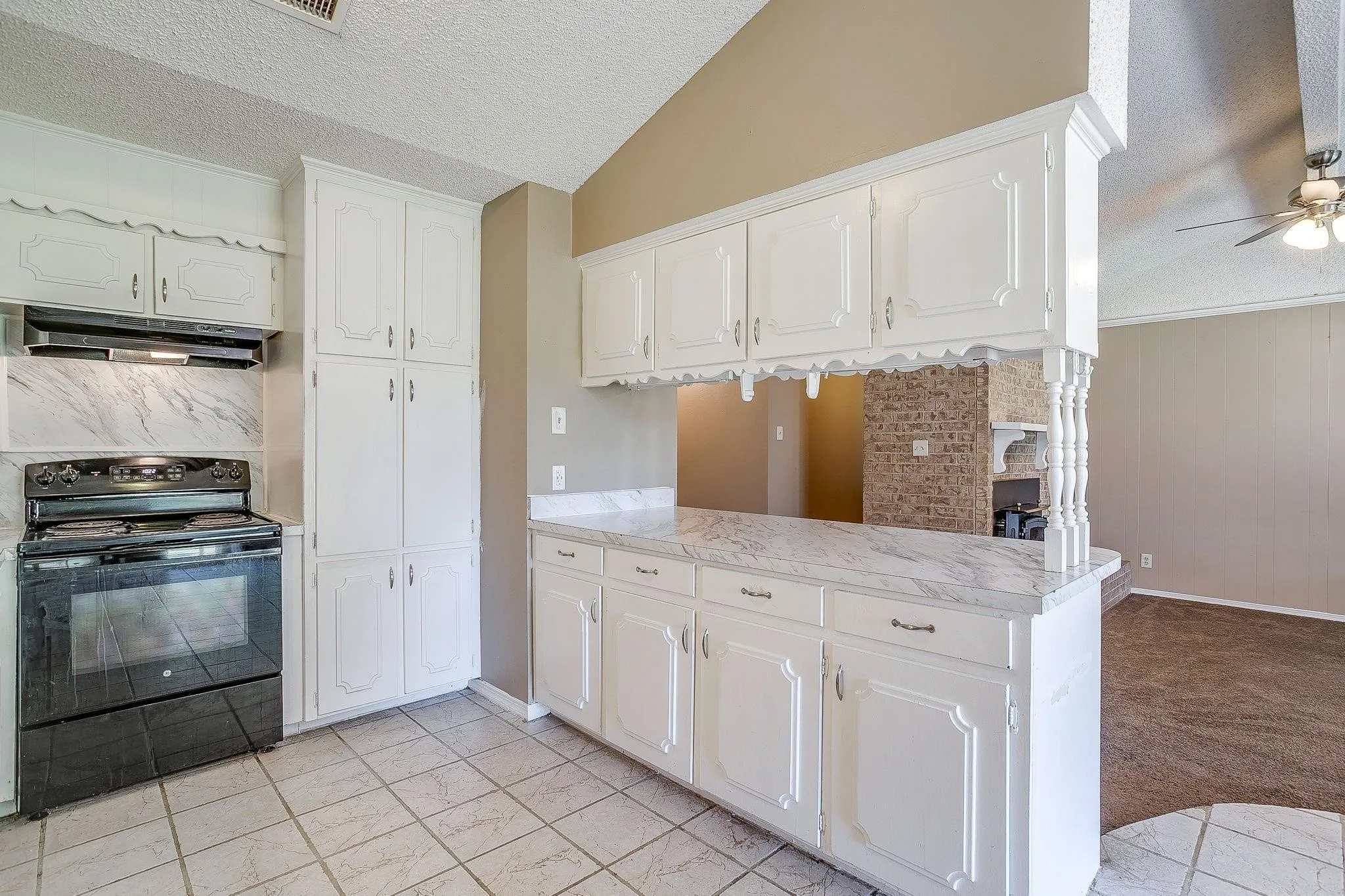 White cabinetry with decorative trim, marbe-finish countertops, tiled flooring, integrated black electric range, and a breakfast bar