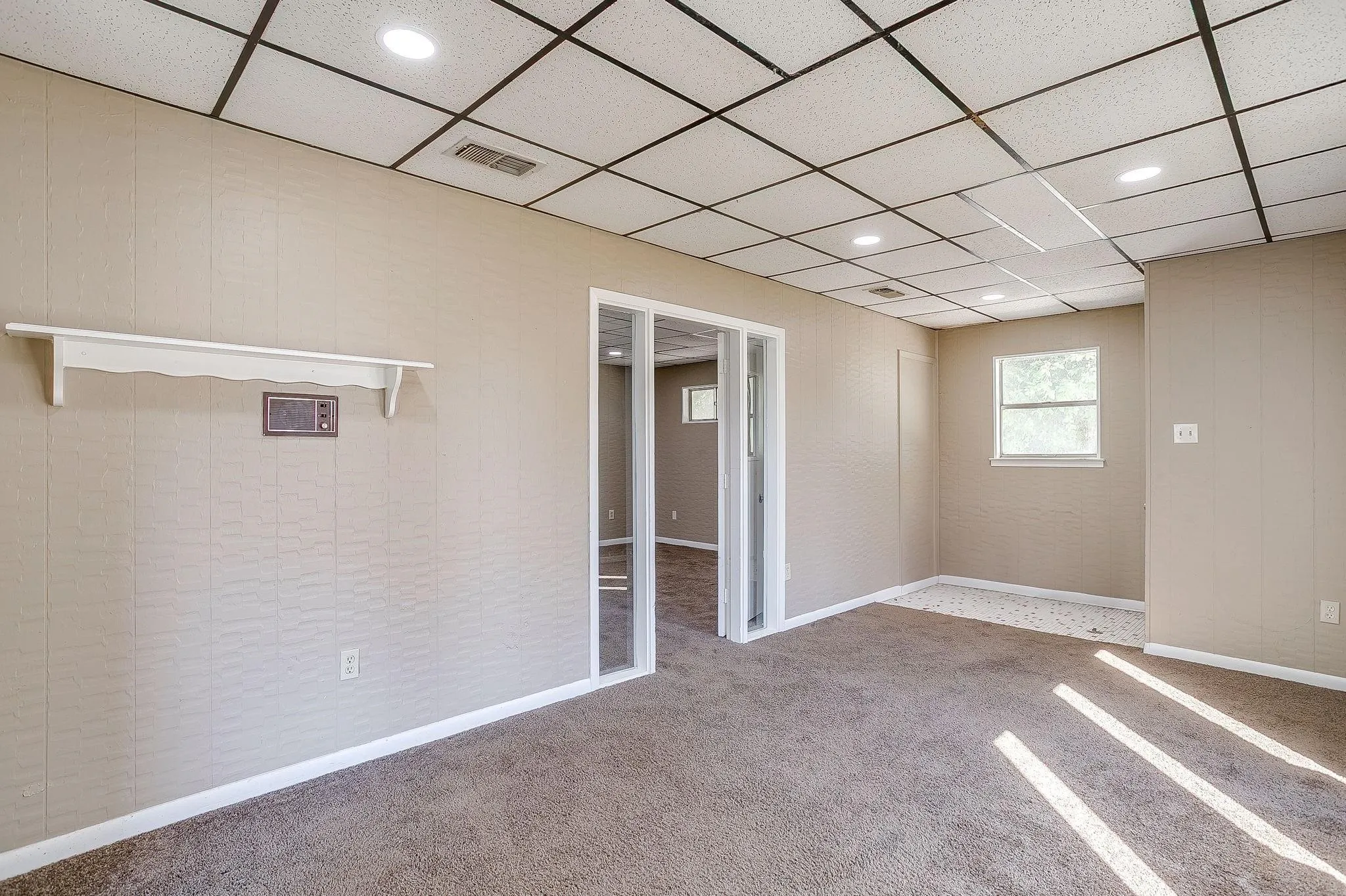 Recessed lighting illuminates the space, featuring a drop ceiling, panel walls, and carpeting