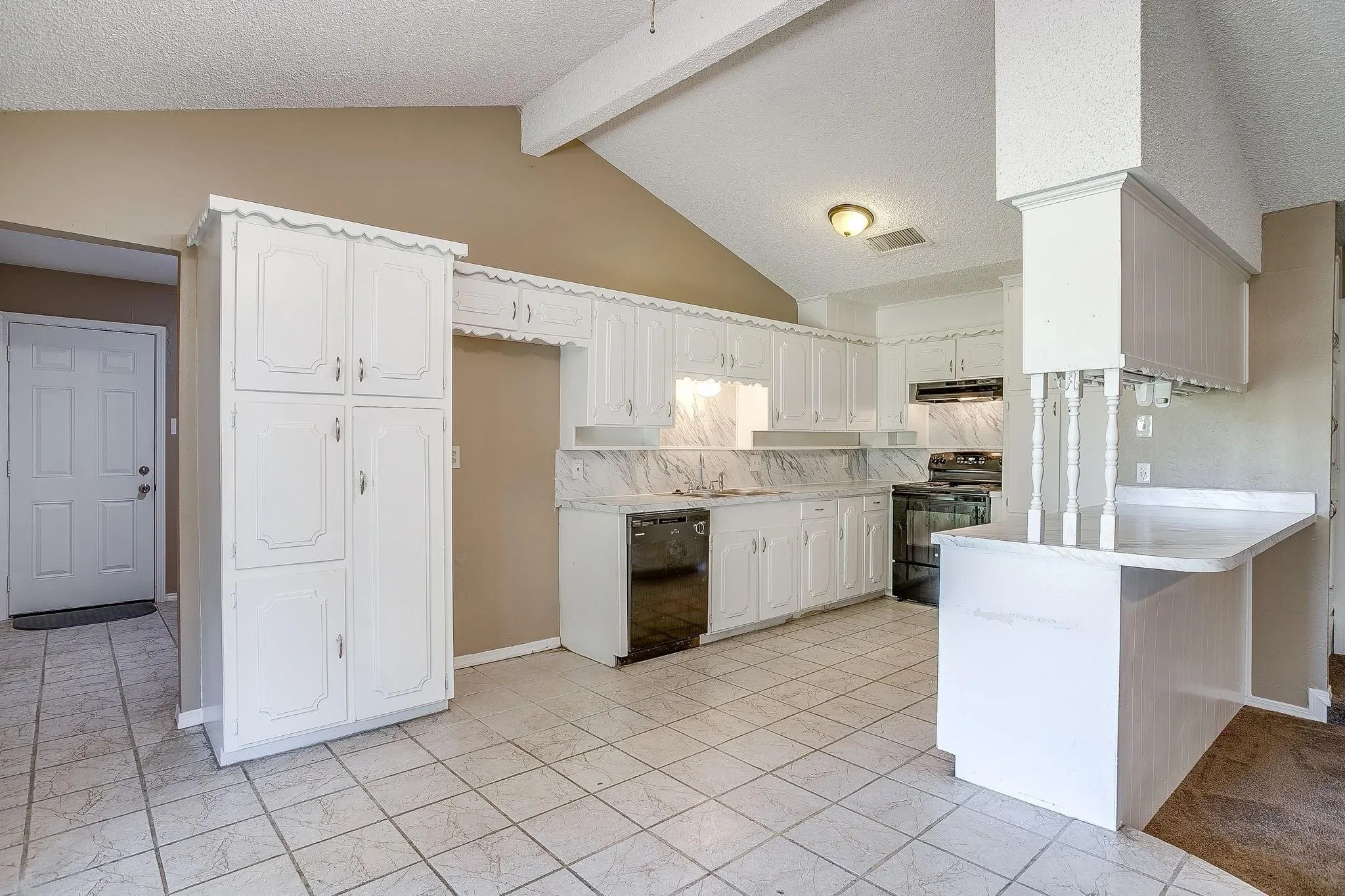 Kitchen featuring vaulted ceilings, white cabinetry, integrated breakfast bar, built-in pantry, and tile flooring