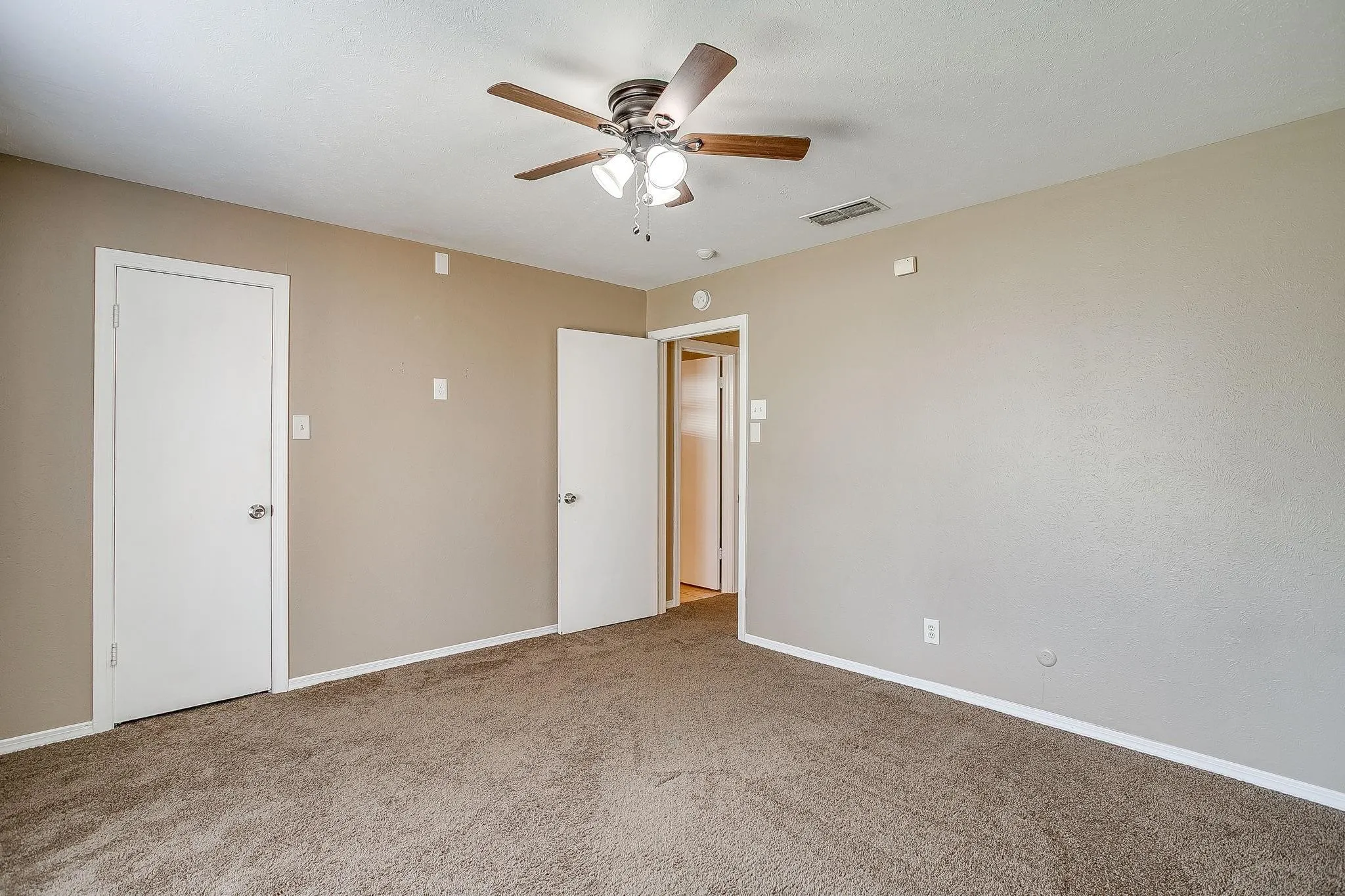 Neutral-toned walls, ceiling fan with light fixture, and carpeted flooring