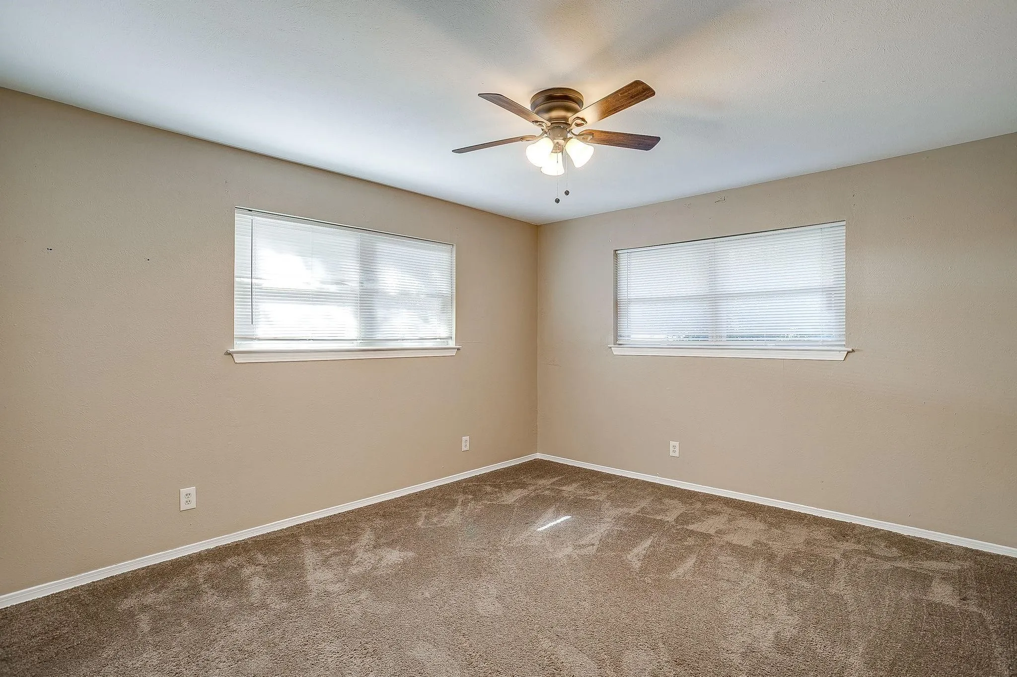 Ceiling fan with integrated lighting, two windows with blinds, and textured carpet flooring
