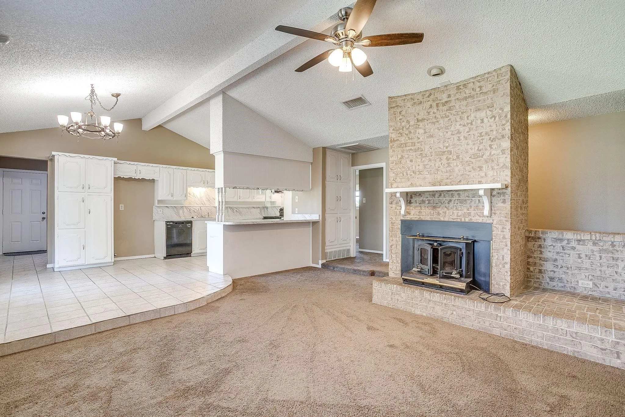 Vaulted ceilings with exposed beams, brick fireplace, ceramic tile flooring, built-in white cabinetry, and a ceiling fan with integrated lighting