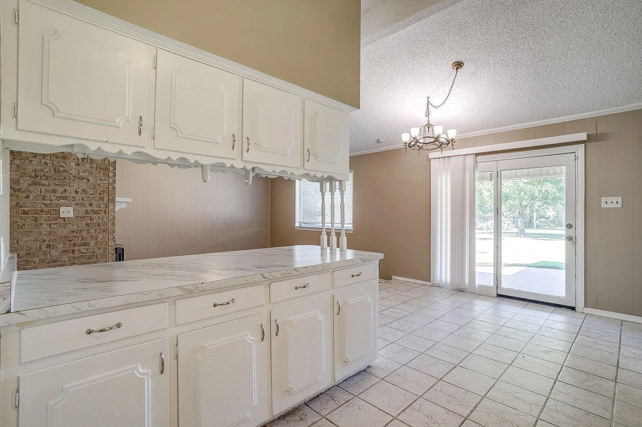 White cabinetry with decorative fronts, light-toned countertop, tile flooring, sliding glass door, and chandelier lighting