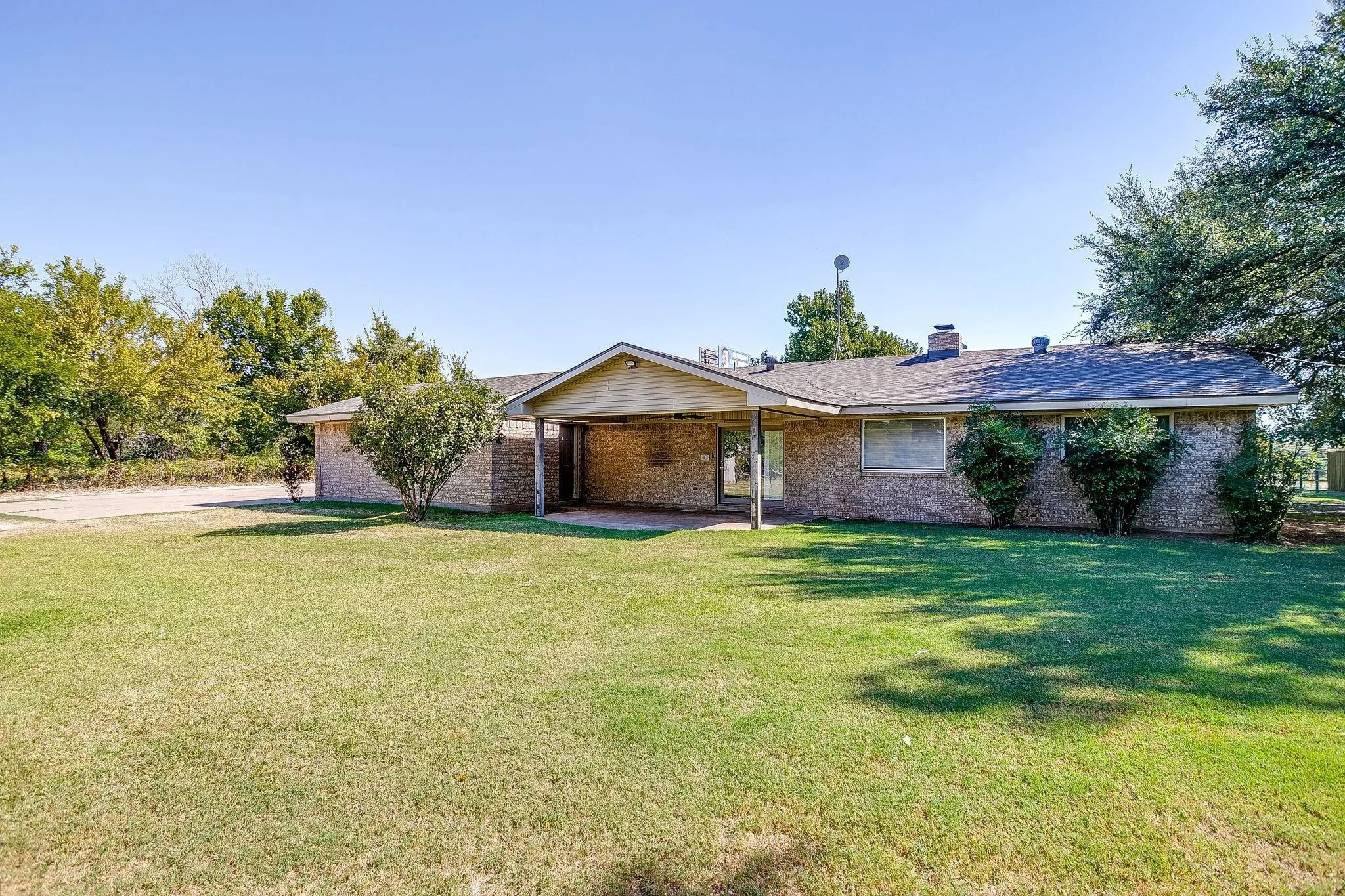 Brick exterior with a covered carport, pitched roof, and established landscaping