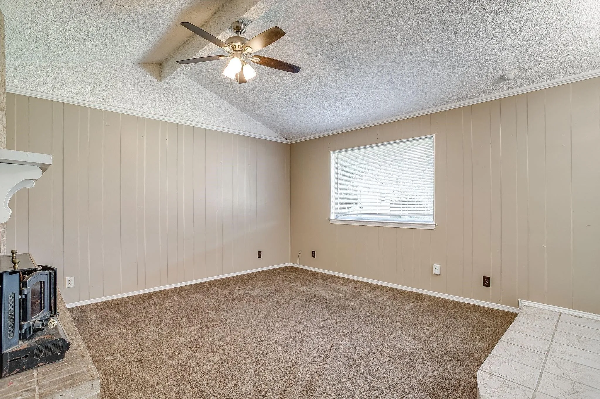 Vaulted ceiling with exposed beams, ceiling fan, carpet flooring, and a fireplace with a stone hearth