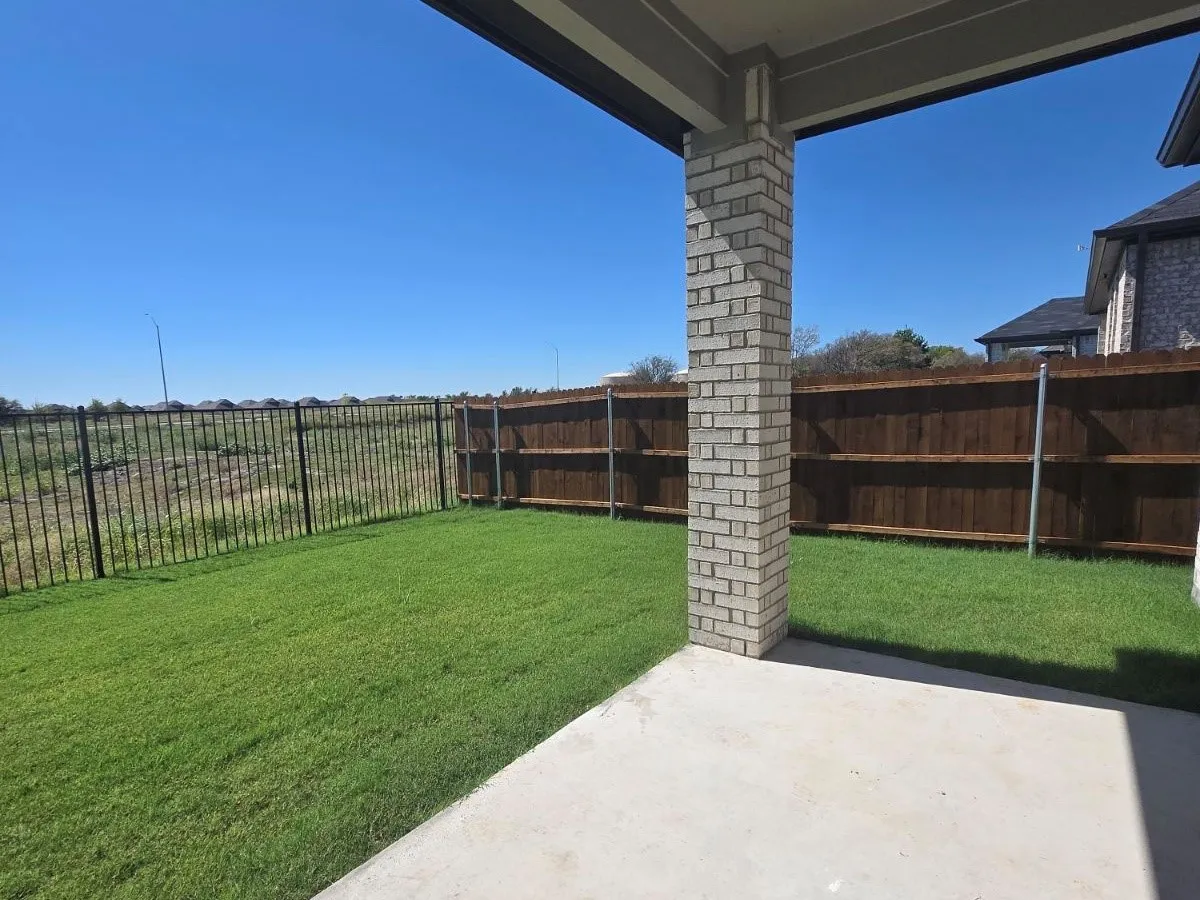 Expansive backyard featuring a concrete patio, brick column support, and a wood privacy fence