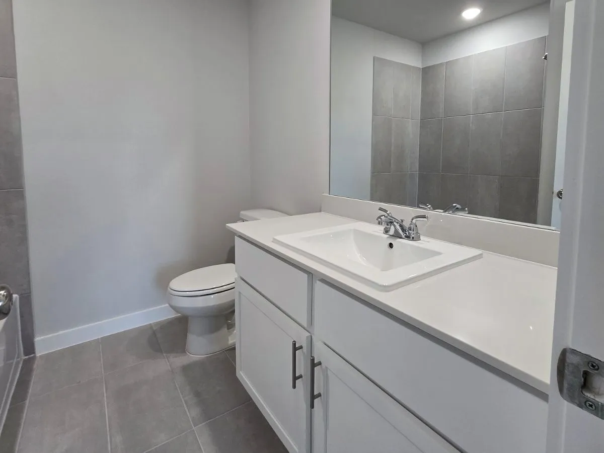 Modern bathroom featuring a white vanity with an integrated sink, polished chrome faucet, rectangular mirror, and large format floor tiling