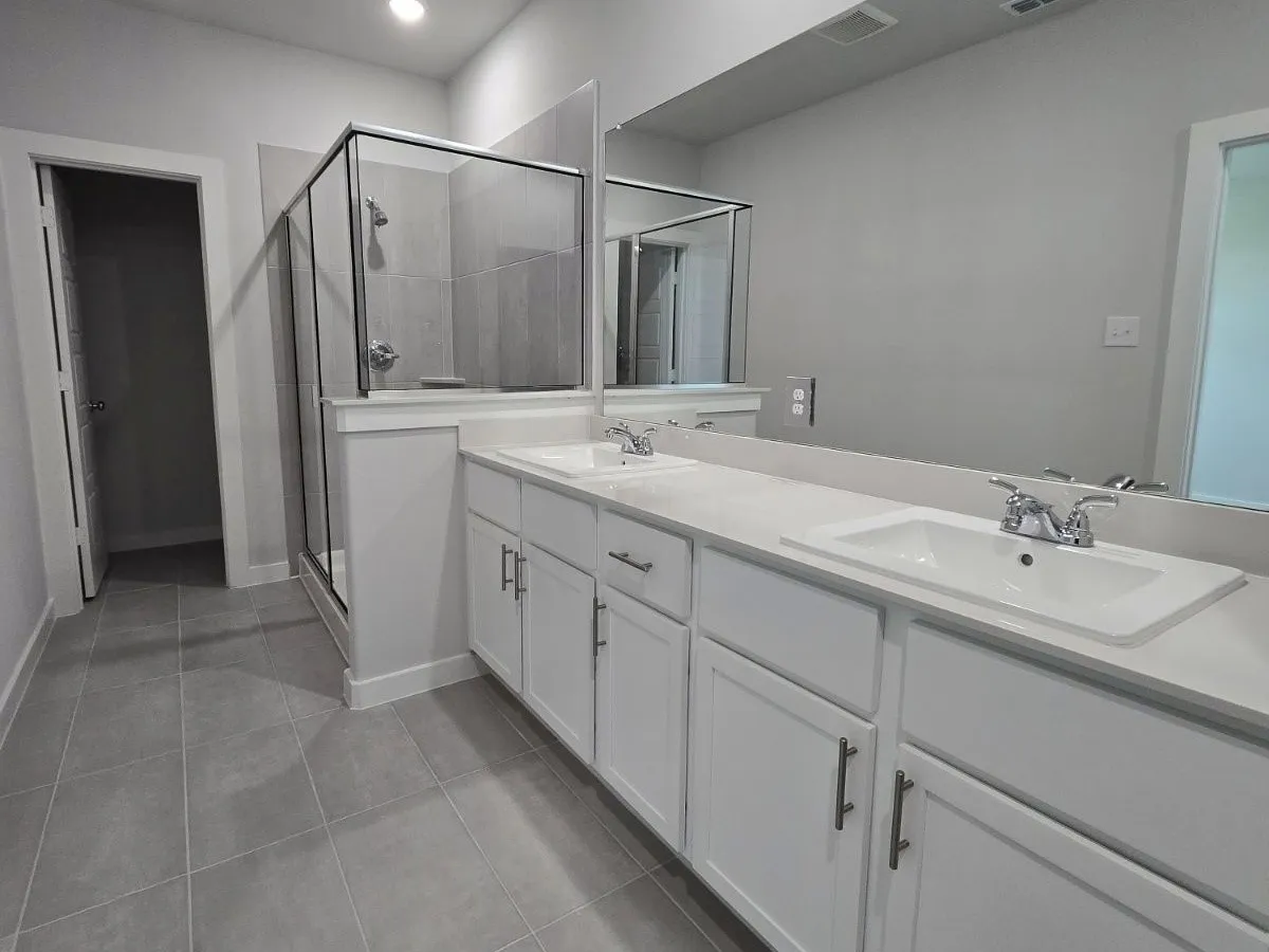 Dual vanity with white cabinetry and integrated sinks, a glass-enclosed shower, and tile flooring