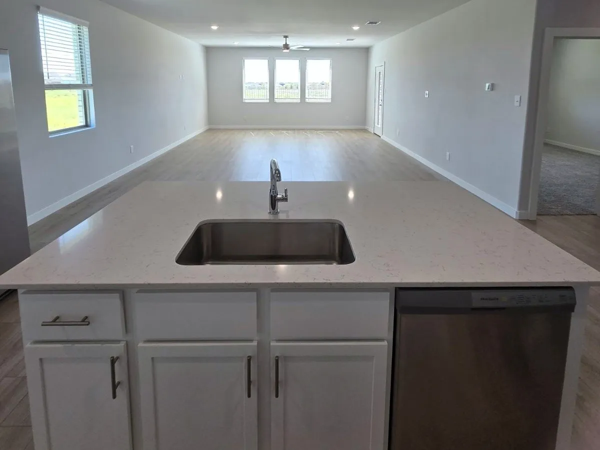 Kitchen island featuring a stainless steel undermount sink, a chrome gooseneck faucet, light-toned countertop, and integrated dishwasher