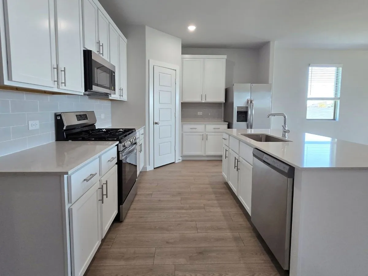 Kitchen featuring wood-finish flooring, white cabinetry, integrated stainless steel appliances, light-toned countertops, and a subway tile backsplash