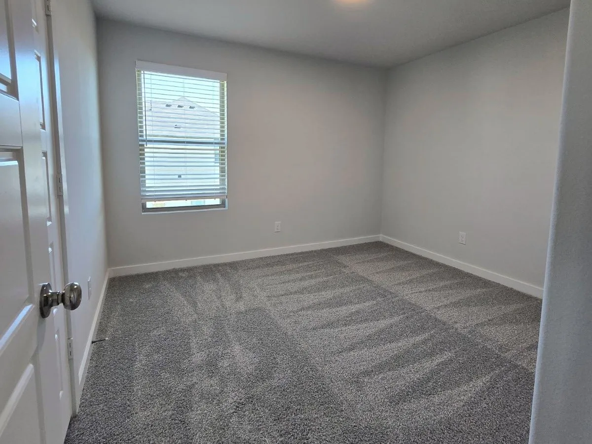 Neutral wall paint, window with blinds, overhead lighting, and patterned carpeting