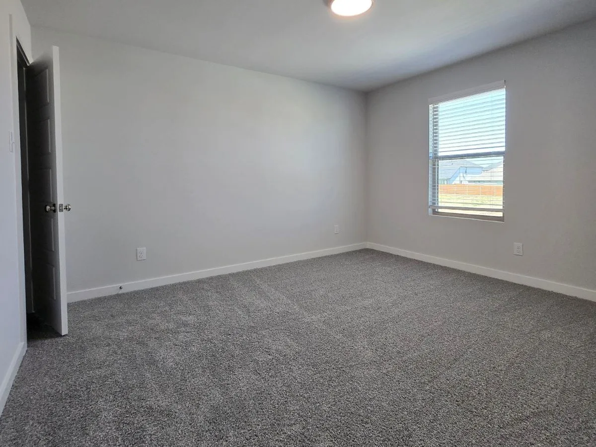 Neutral-toned carpeting, light gray wall paint, and a single window with horizontal blinds