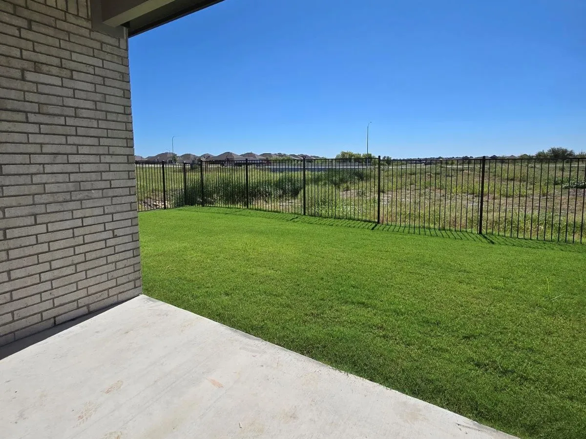 Manicured lawn with a concrete patio, brick exterior, and black metal fencing