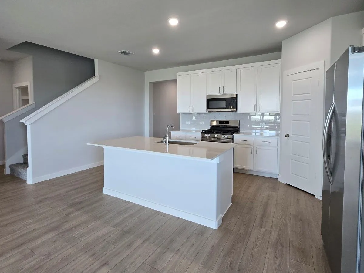 Open-concept kitchen featuring white cabinetry, stainless steel appliances, a center island with sink, and wood-finish flooring