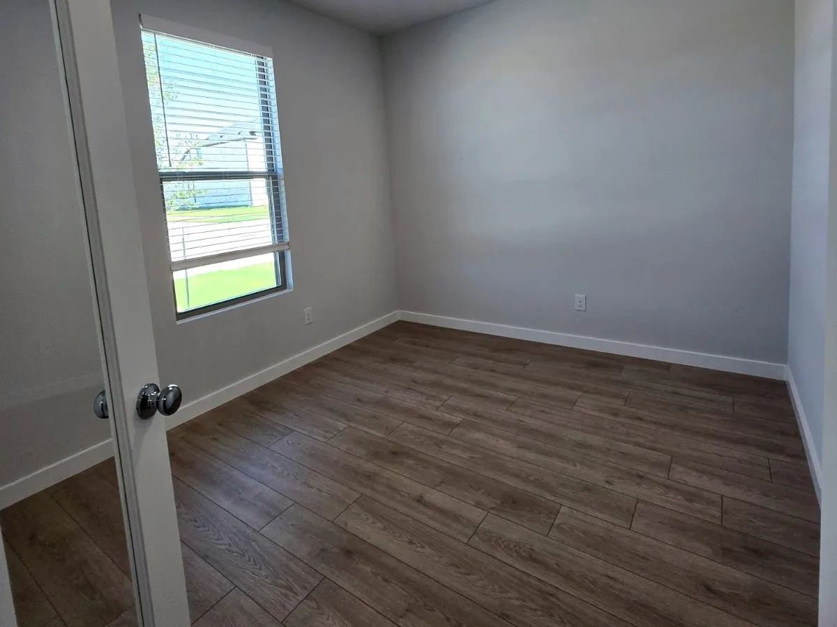 Wood-finish flooring, white wall paint, window with blinds, white trim, and a chrome doorknob