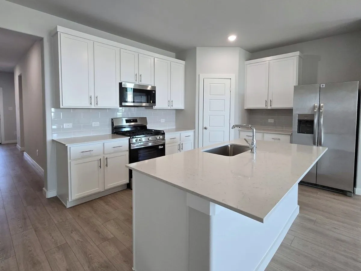 Kitchen featuring white cabinetry, stainless steel appliances, light-toned countertops, subway tile backsplash, and wood-finish flooring