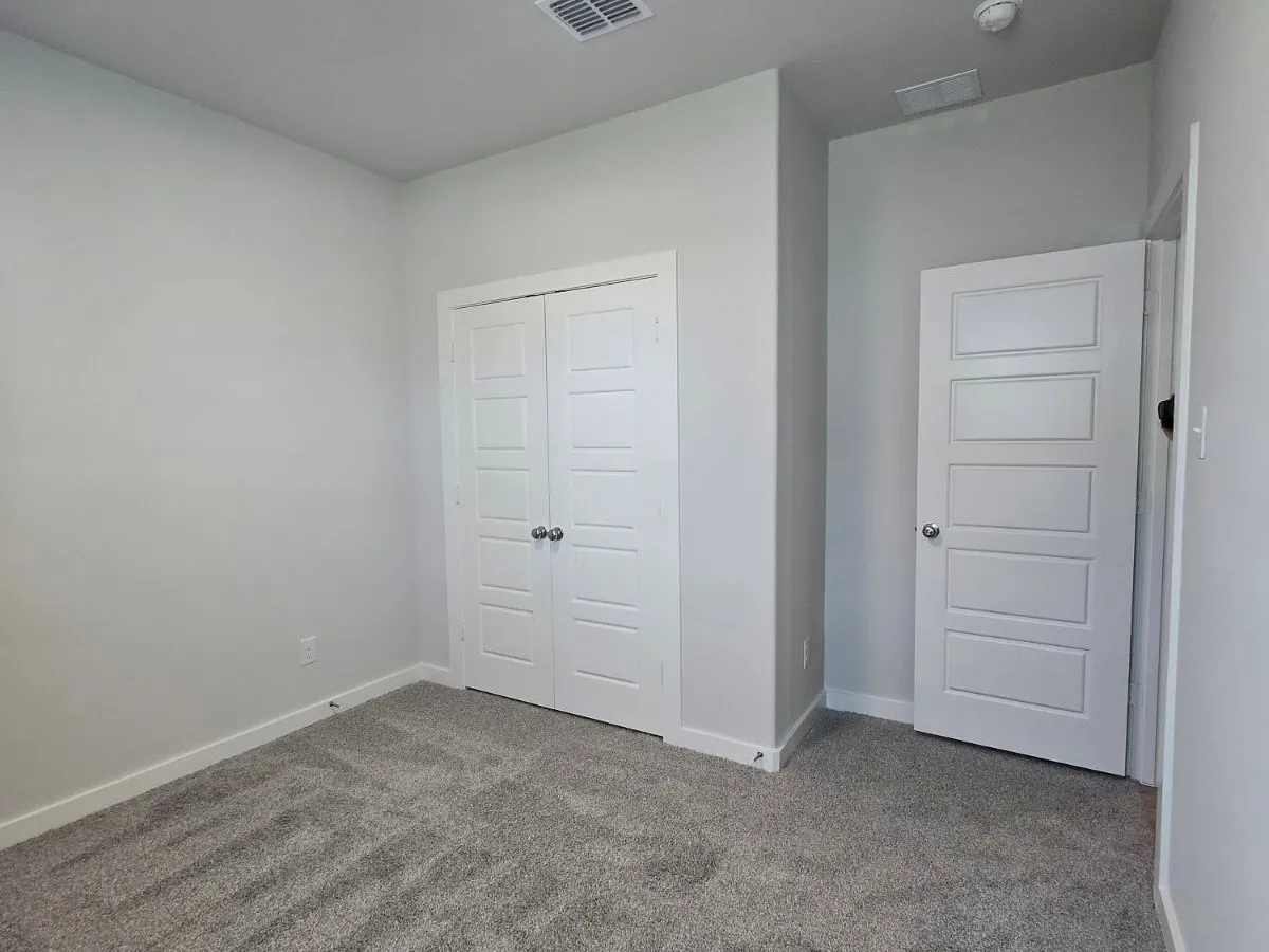 Wall-to-wall carpeting in a neutral tone, white baseboards, and two paneled doors with chrome hardware