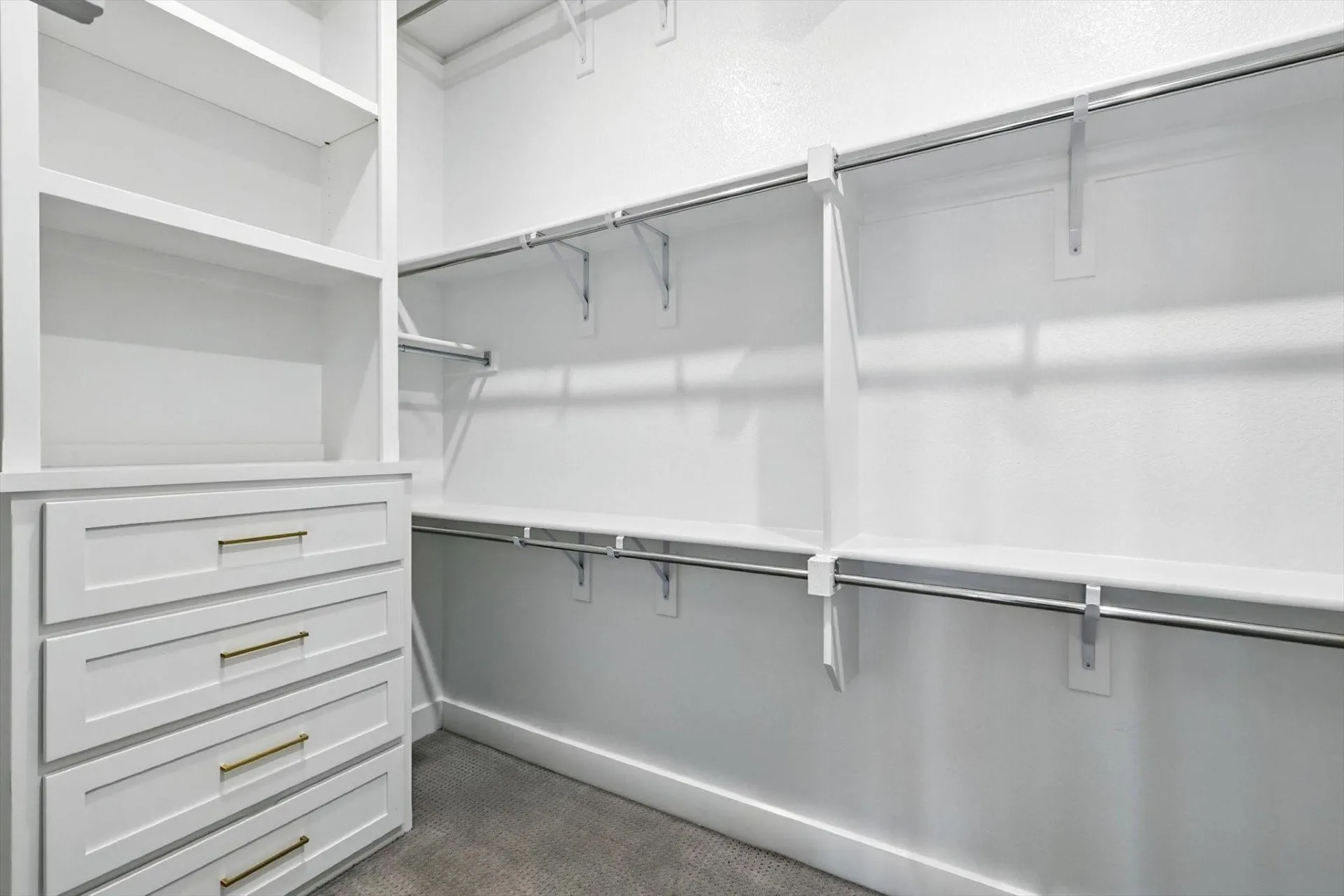 Custom built-in shelving, integrated drawers with gold-tone hardware, multiple hanging rods, white-painted walls, and gray carpeting