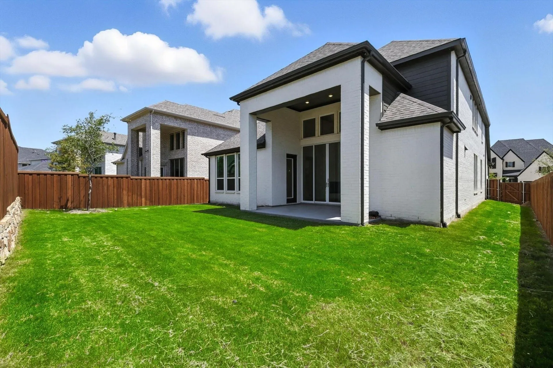 Expansive backyard featuring a manicured lawn, wood fencing, and a stone retaining wall