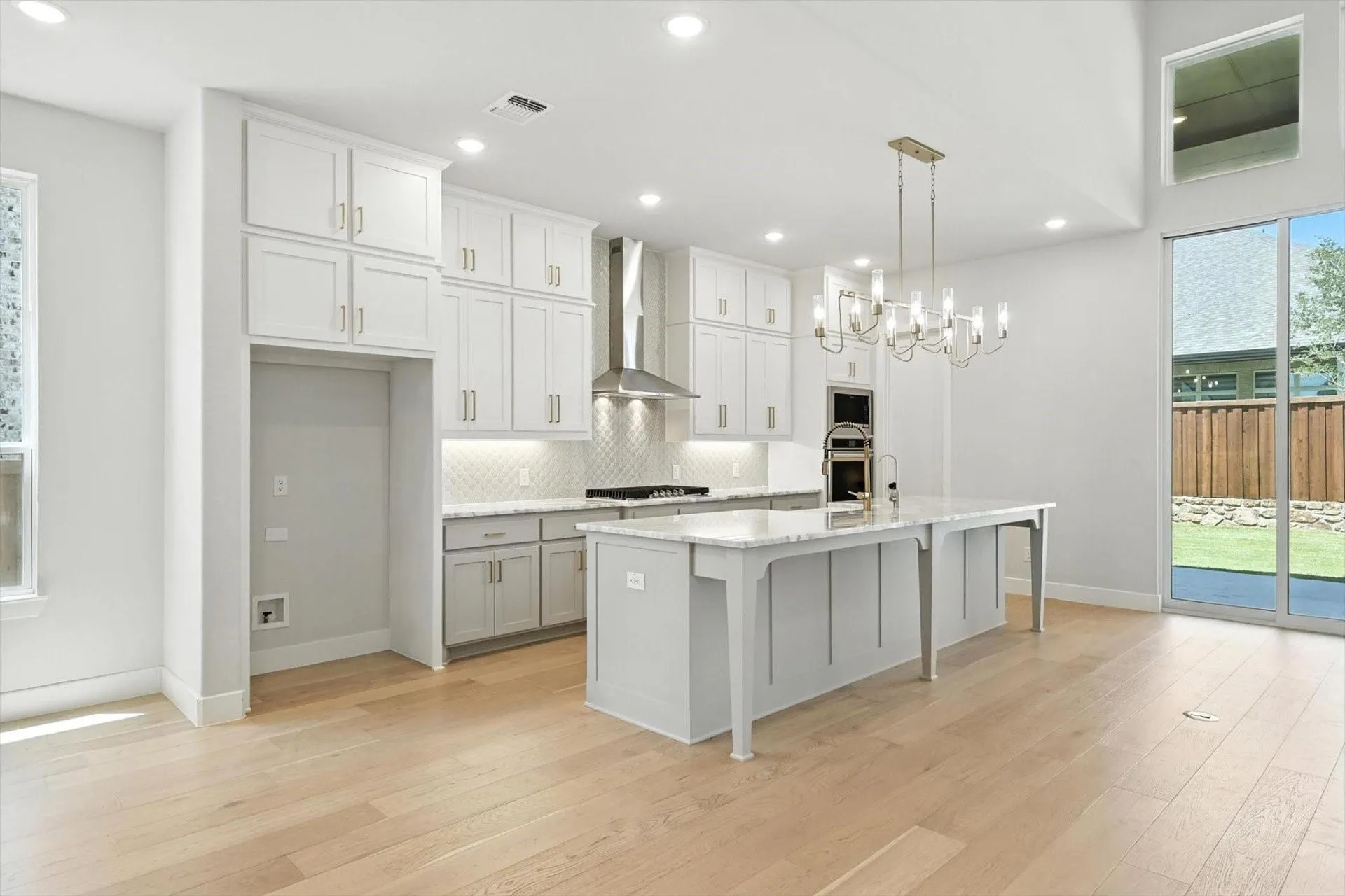 Gourmet kitchen with light wood-finish flooring, white cabinetry, a large central island with a stone countertop, a stainless steel range hood, and integrated double ovens