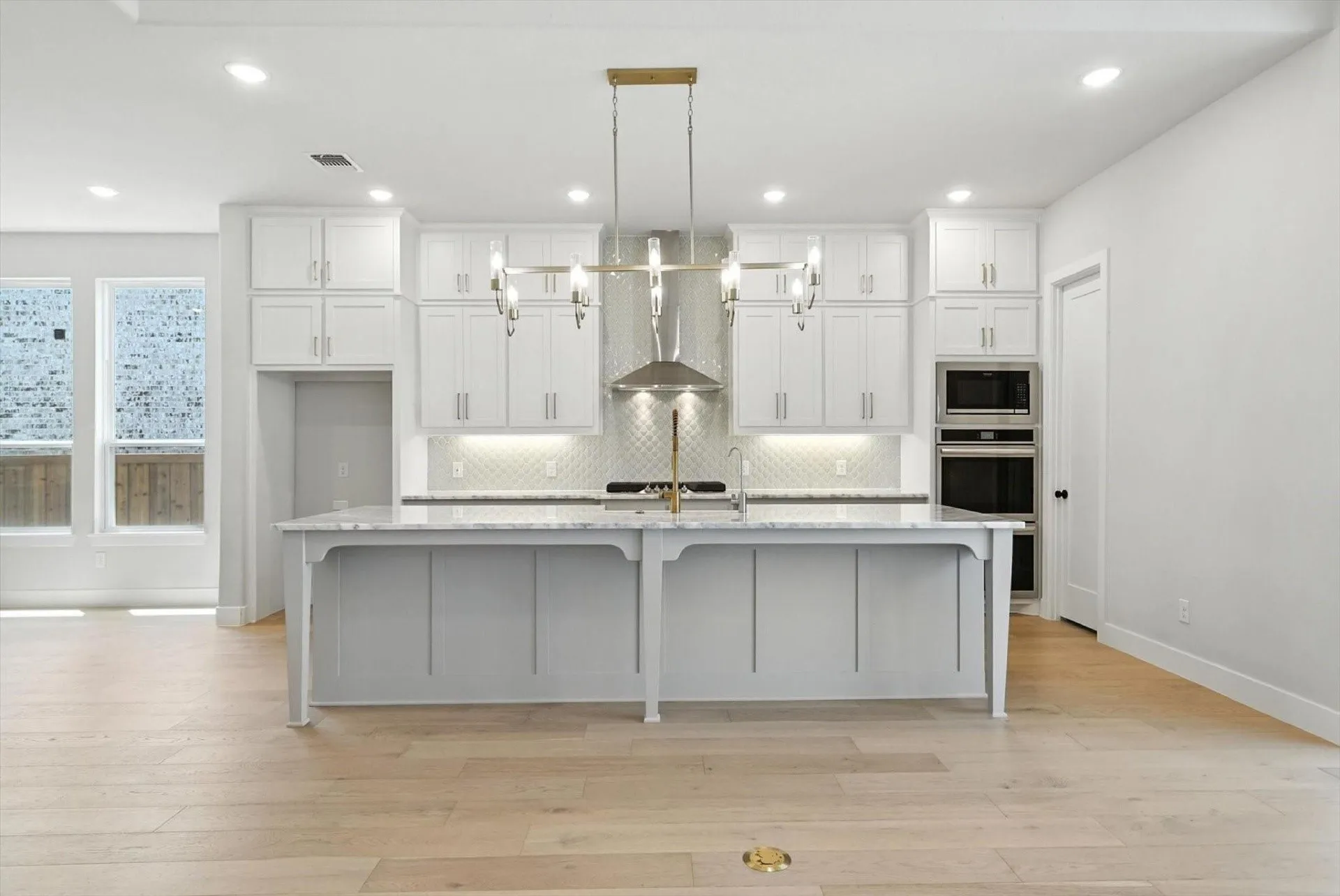 Expansive kitchen island with a stone countertop, abundant white cabinetry, stainless steel appliances, and wood-finish flooring