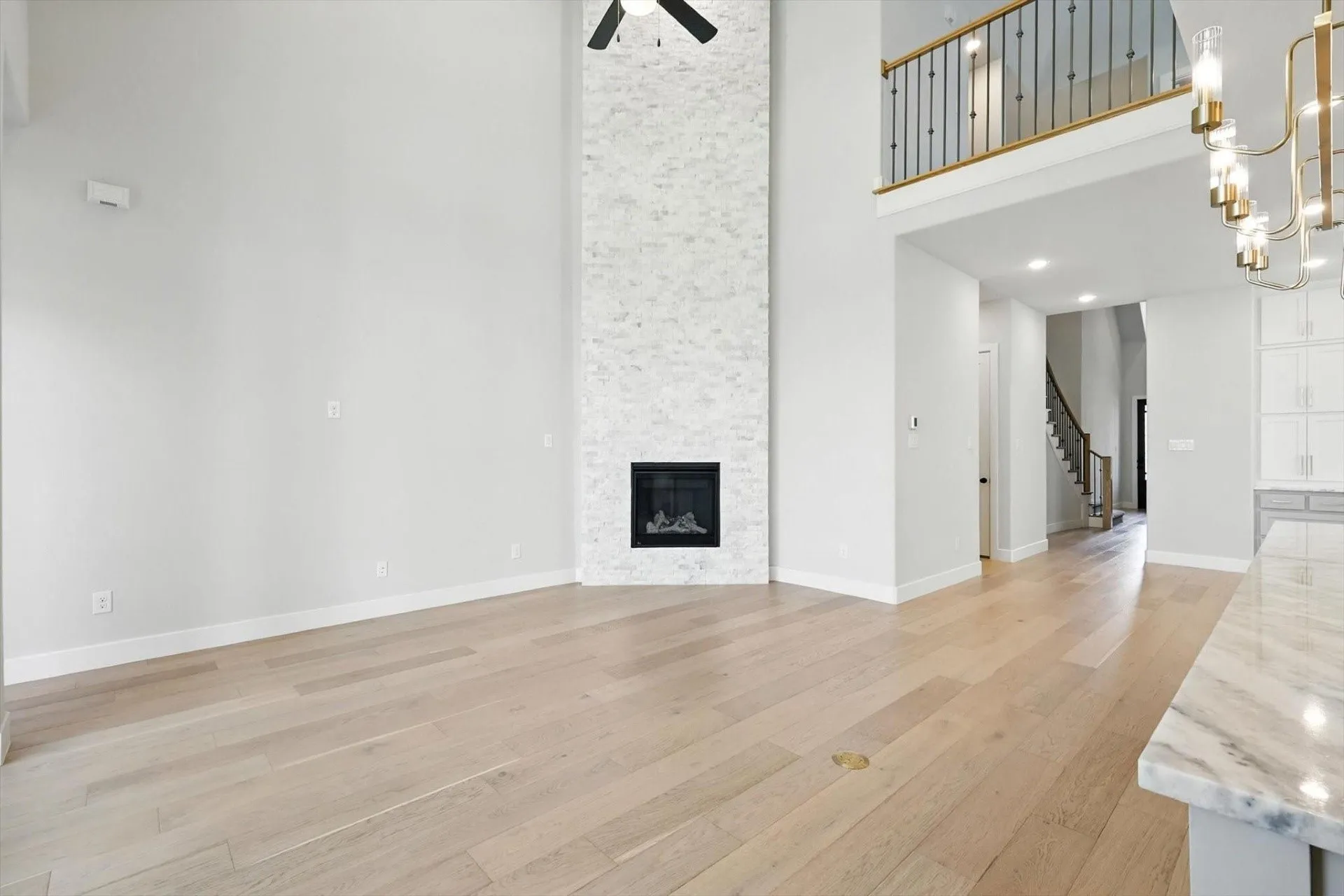 Soaring ceilings with a black ceiling fan, stone-clad fireplace, light wood-finish flooring, and a marble-finish countertop