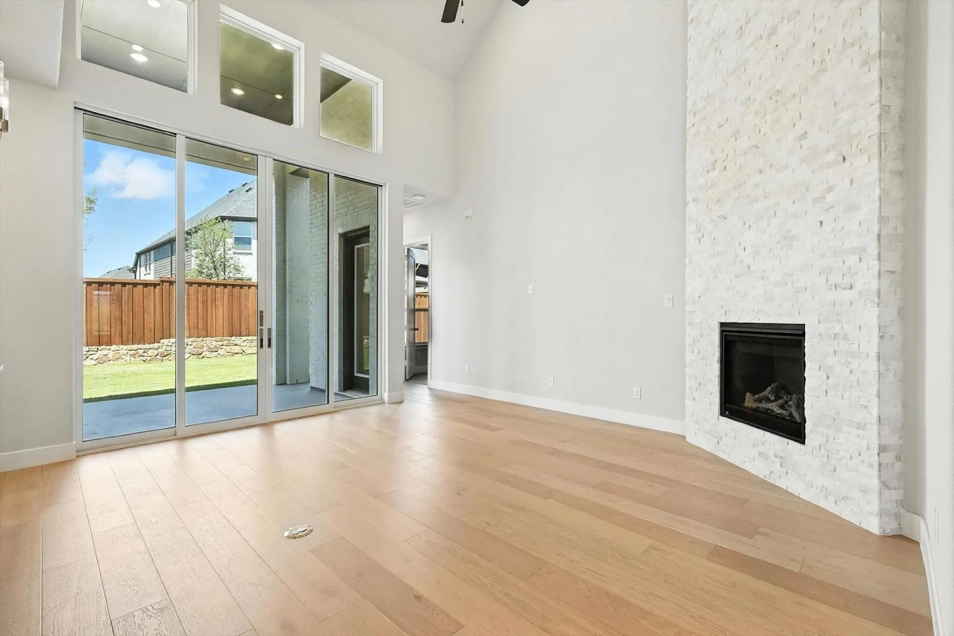 Vaulted ceiling with a ceiling fan, white stacked stone fireplace, wood-finish flooring, and a sliding glass door to the backyard