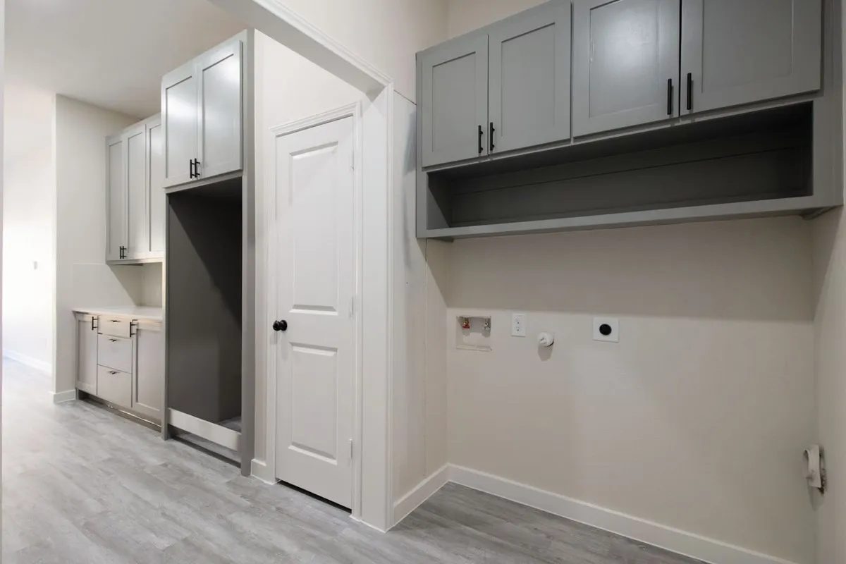 Wood-finish flooring, built-in cabinetry with matte black hardware, integrated appliance space, and dedicated laundry hookups