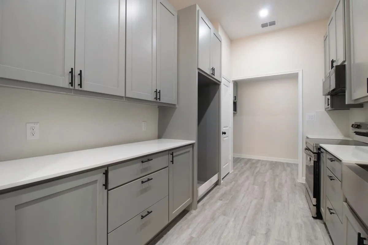Galley kitchen featuring shaker-style cabinetry with matte black hardware, light-toned countertops, and wood-finish flooring