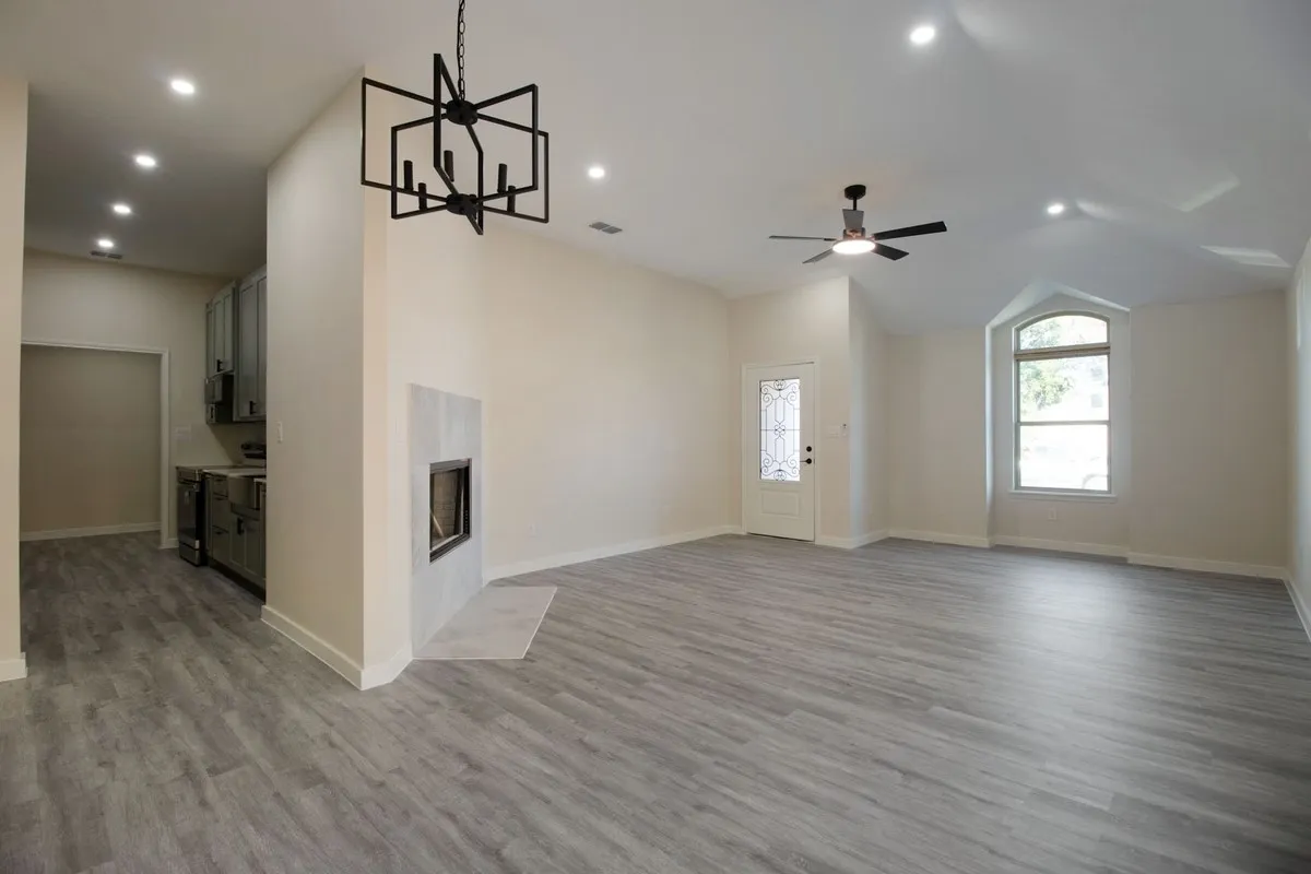 Spacious room featuring wood-finish flooring, a contemporary fireplace with a light-toned surround, a modern chandelier, and recessed lighting