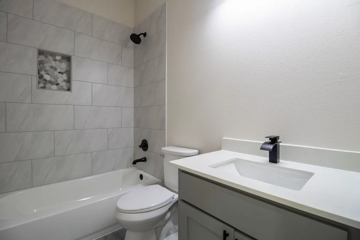 Bathtub with tiled surround and integrated niche, matte black fixtures, vanity with integrated sink, and white countertop