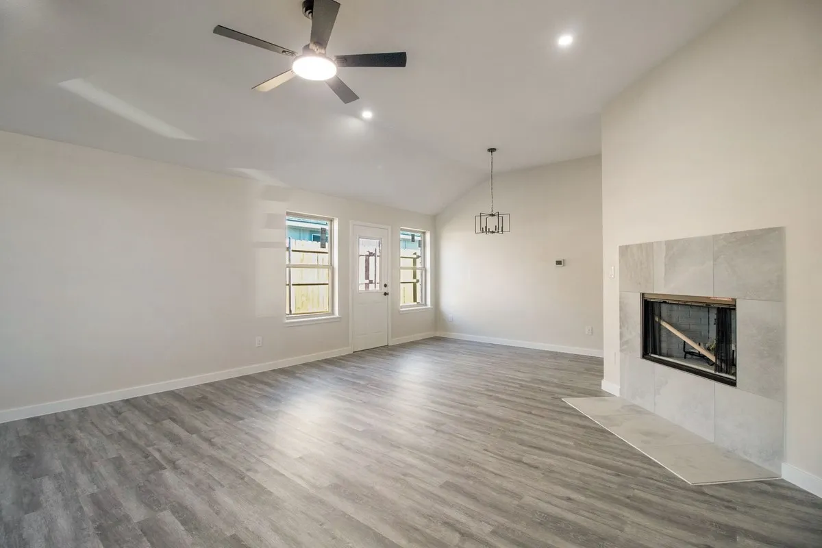 Vaulted ceiling, wood-finish flooring, white walls, built-in fireplace with tile surround, and an exterior door with integrated windows