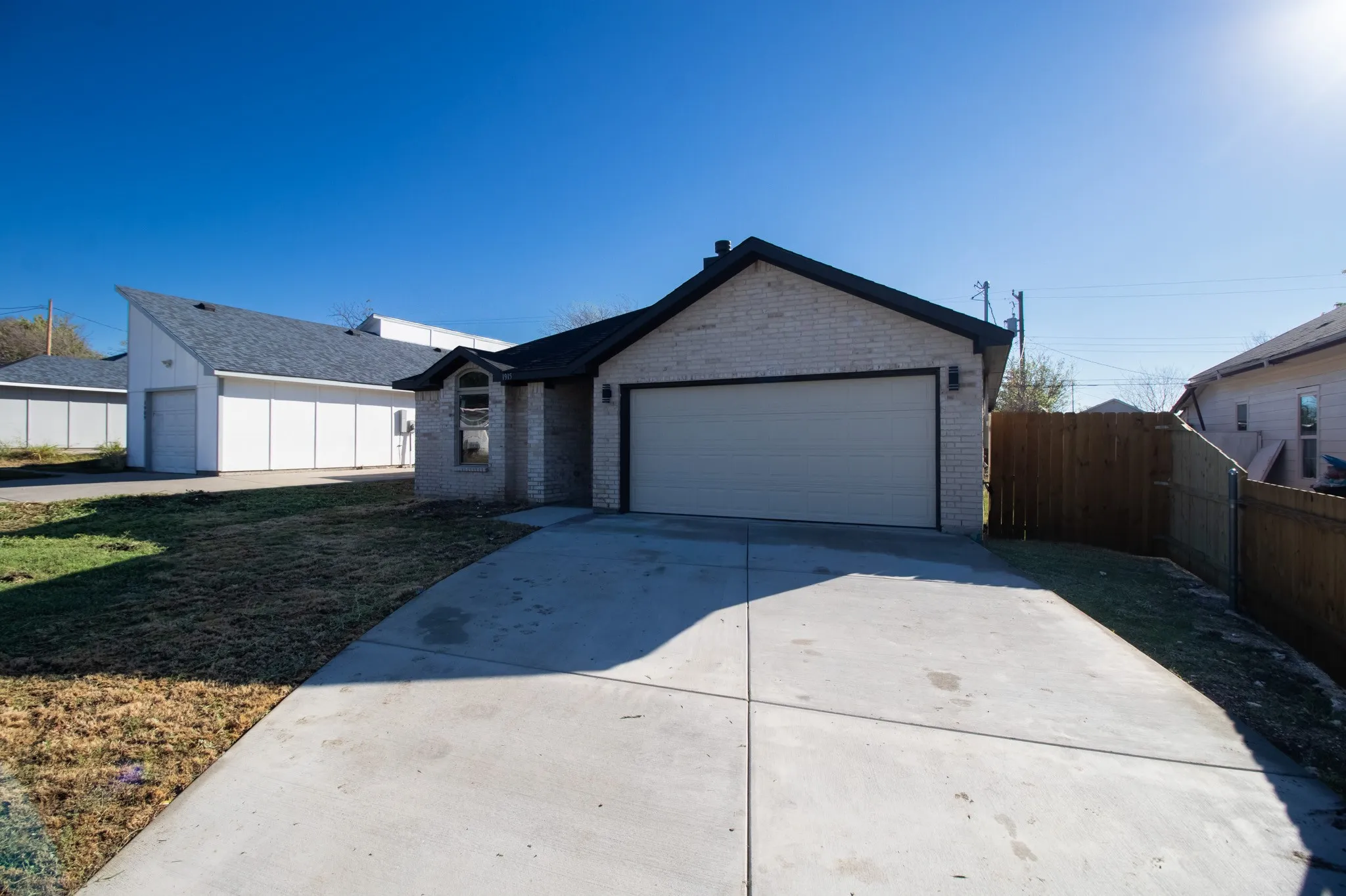 Brick exterior with contrasting dark trim, integrated garage with a light-toned door, concrete driveway, and wood fencing