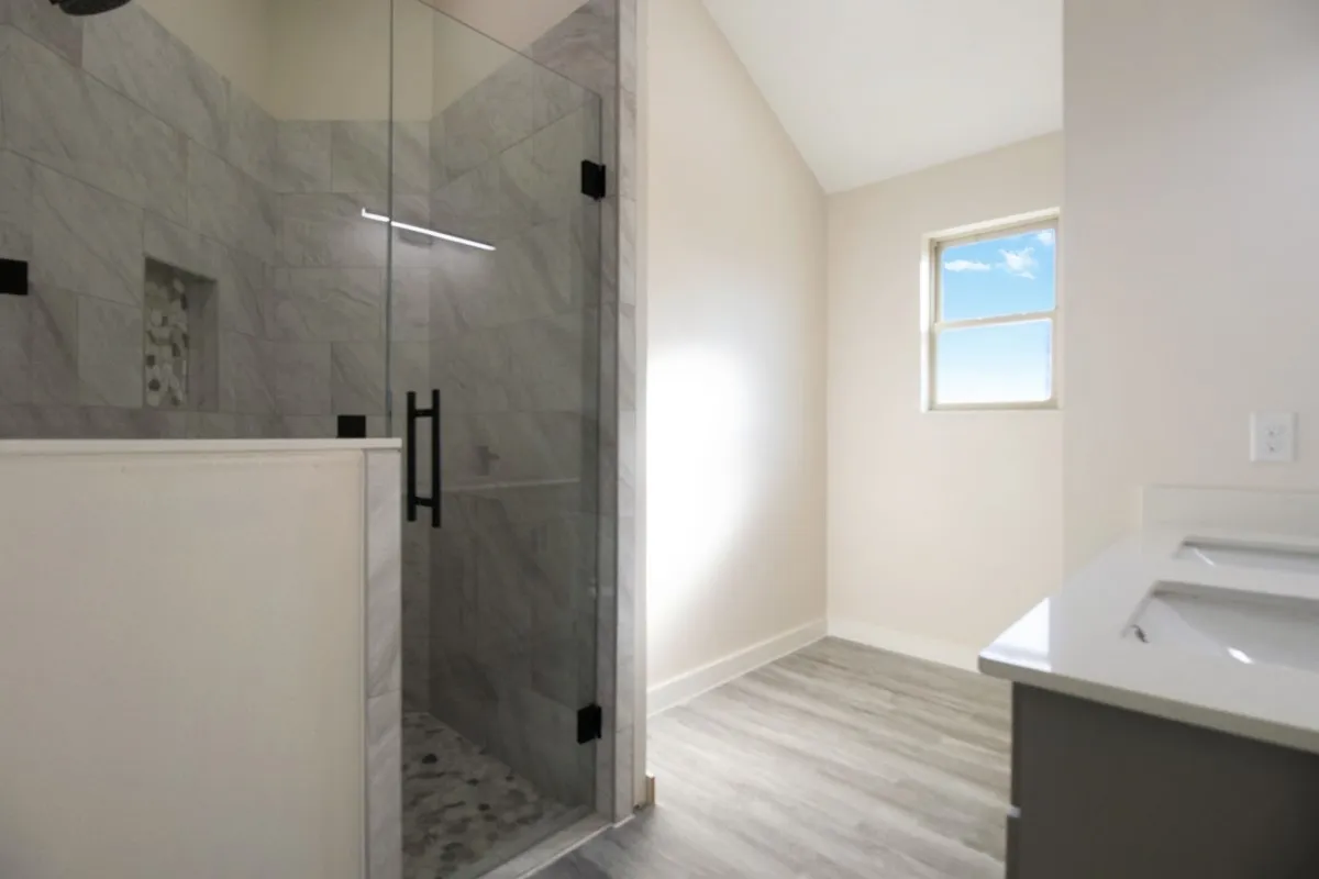 Glass-enclosed shower with tiled walls, stone pebble floor, and integrated niche