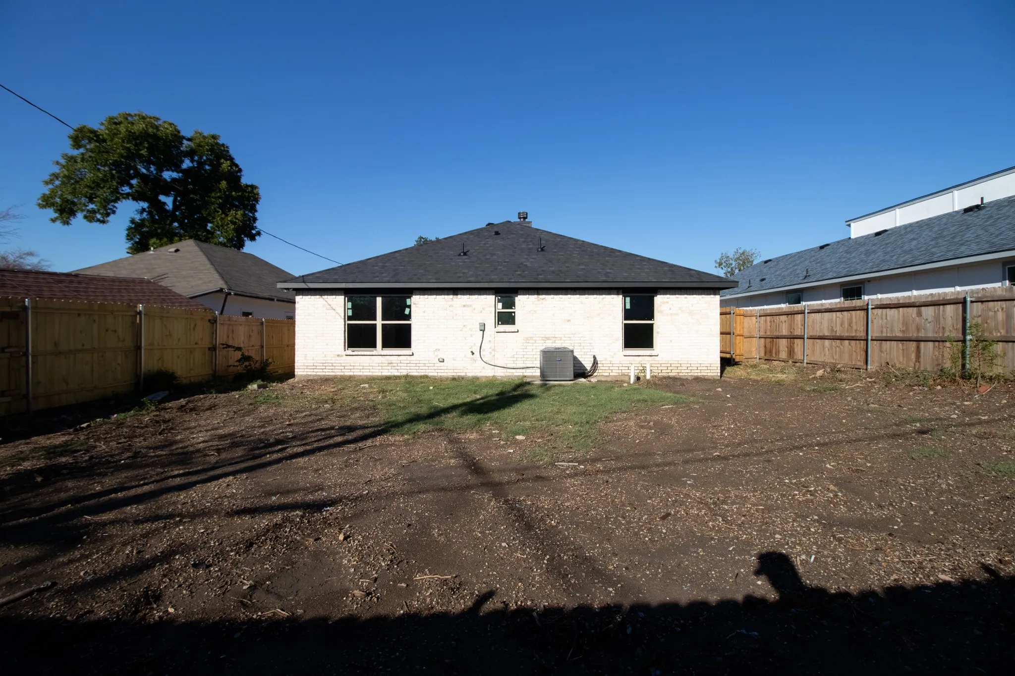 White brick exterior with a dark shingled roof, featuring multiple windows and a rear entry