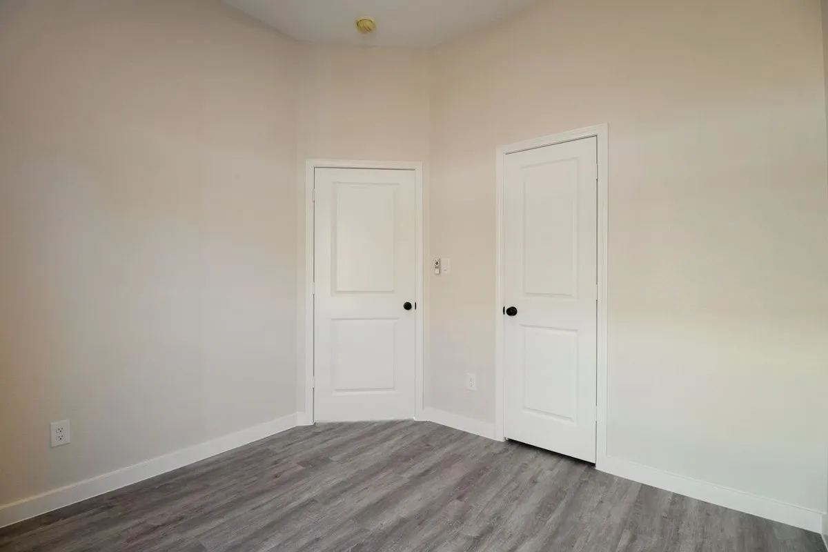 Light-toned walls, two panel doors with matte black hardware, and wood-finish flooring