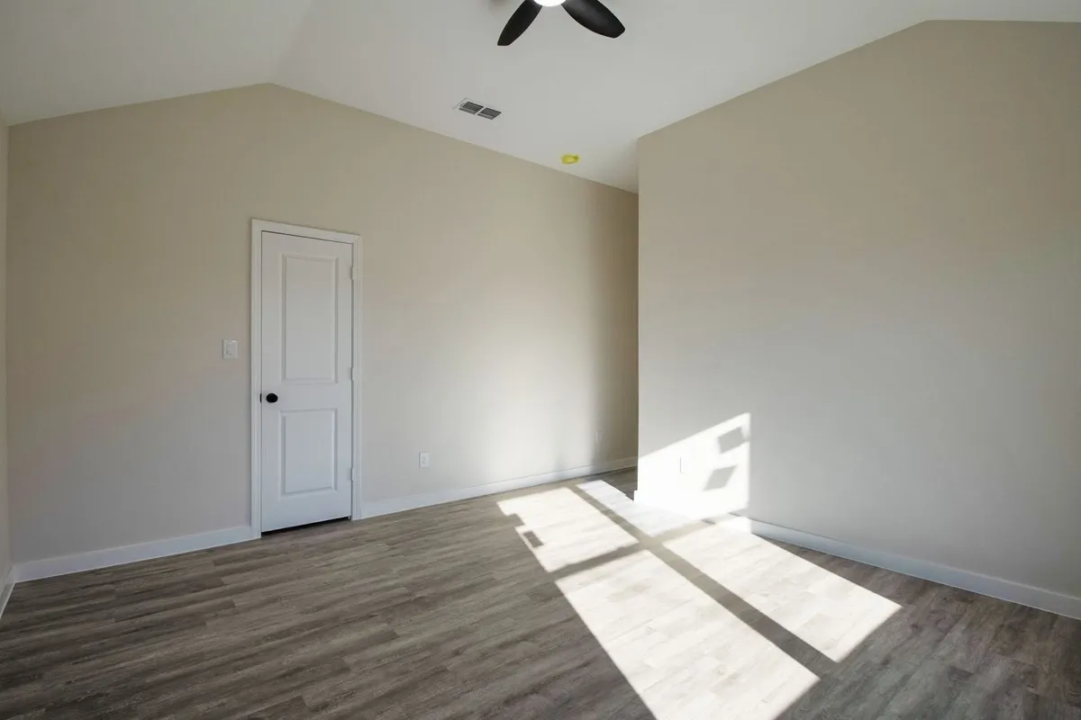 Bright, light-filled bedroom with wood-finish flooring, vaulted ceiling with ceiling fan, and white six-panel closet door