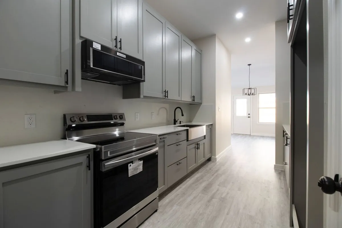 Kitchen featuring light gray cabinetry, stainless steel appliances, white countertops, and a farmhouse sink