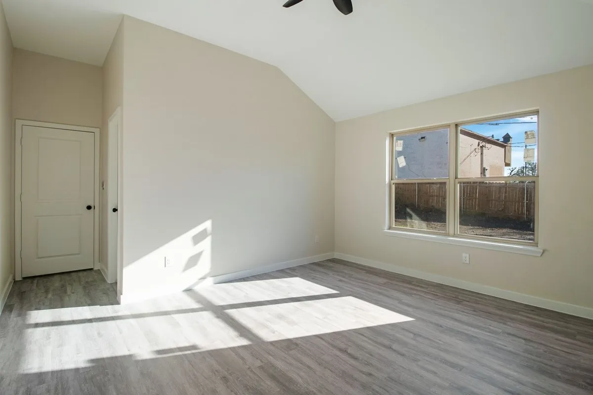 Vaulted ceiling, two-panel interior door, single-pane window, wood-finish flooring, and a ceiling fan
